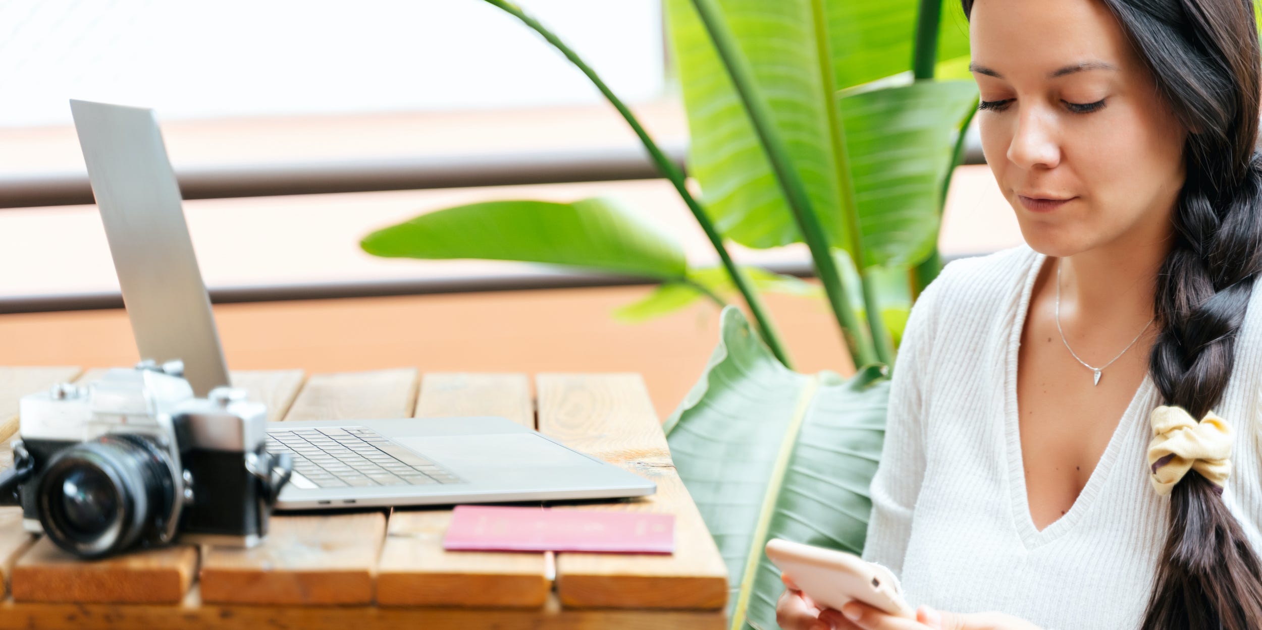 photographer using phone and laptop at desk with camera next to her