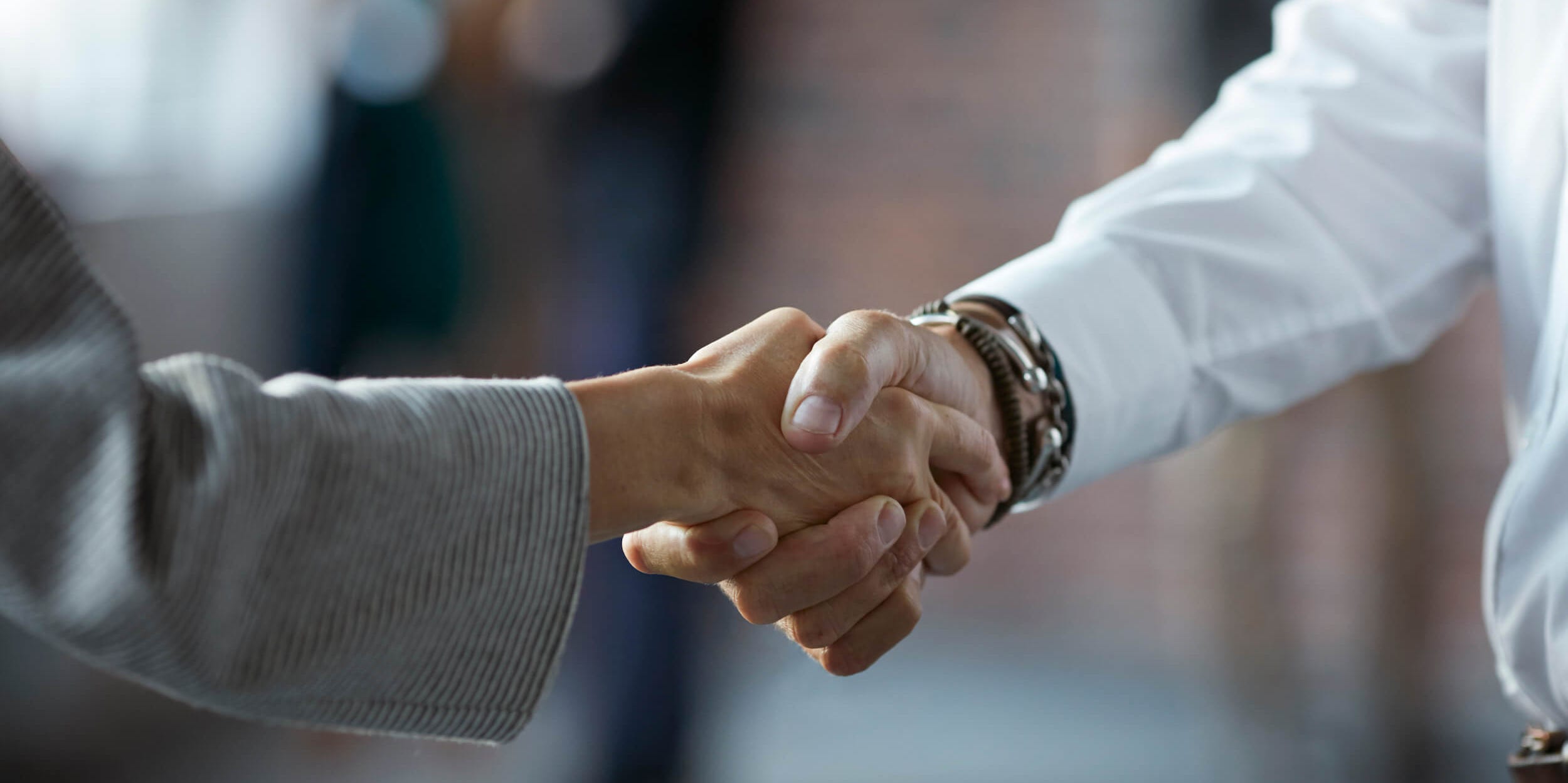 Two business people shaking hands at a conference with a blurred background.