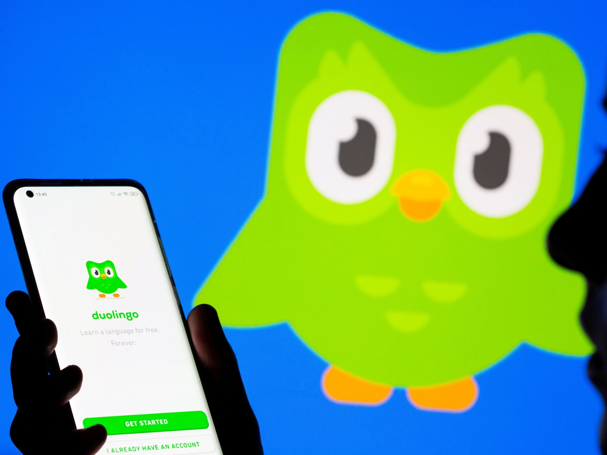 Woman with her smartphone poses in front of displayed Duolingo logo