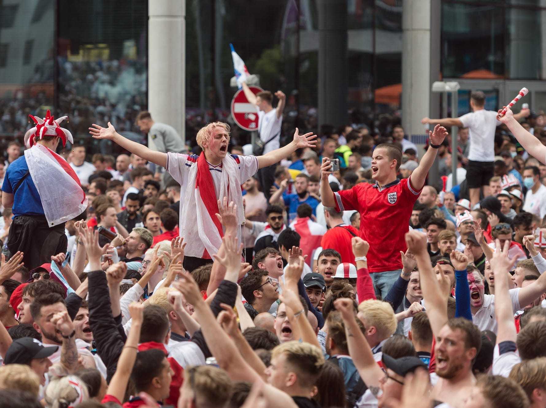 people wearing England football colours are lifted over a packed crowd celebrating a their team at the Euro 2020 championships