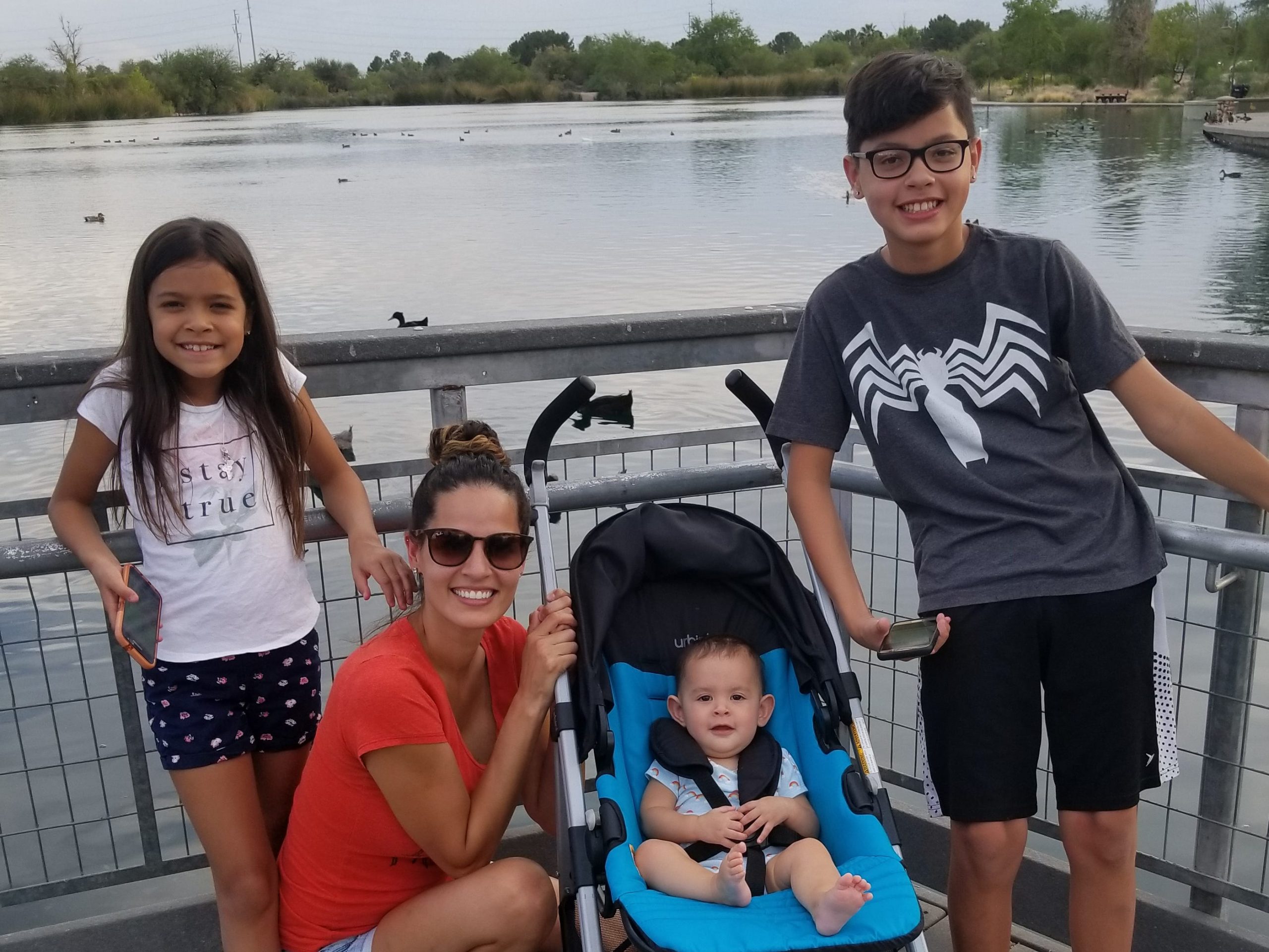 abie standing in front of a lake with mom, sister, and baby sister in stroller