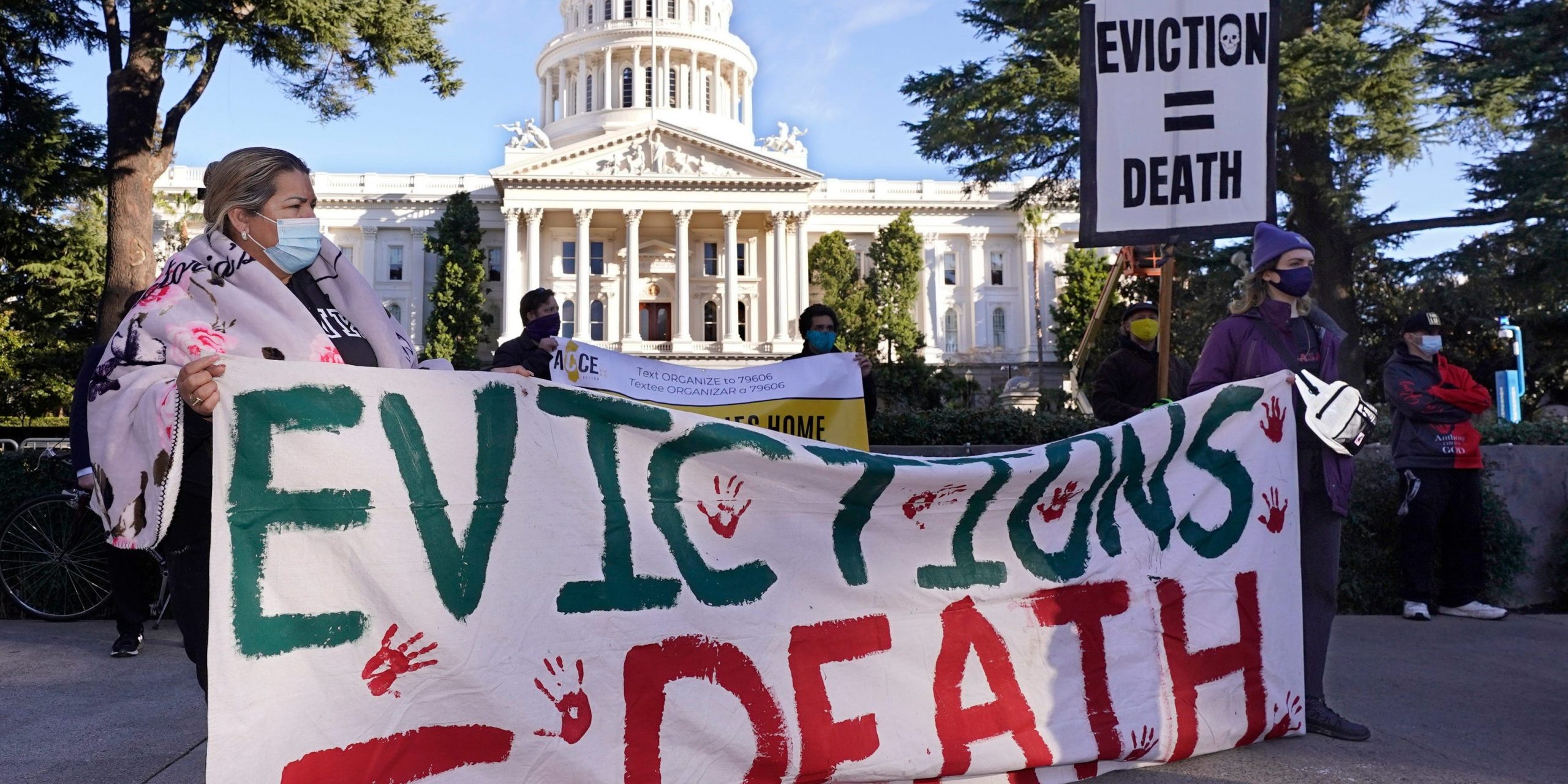 Protesters outside the California Capitol hold a sign that reads "Evictions=Death."