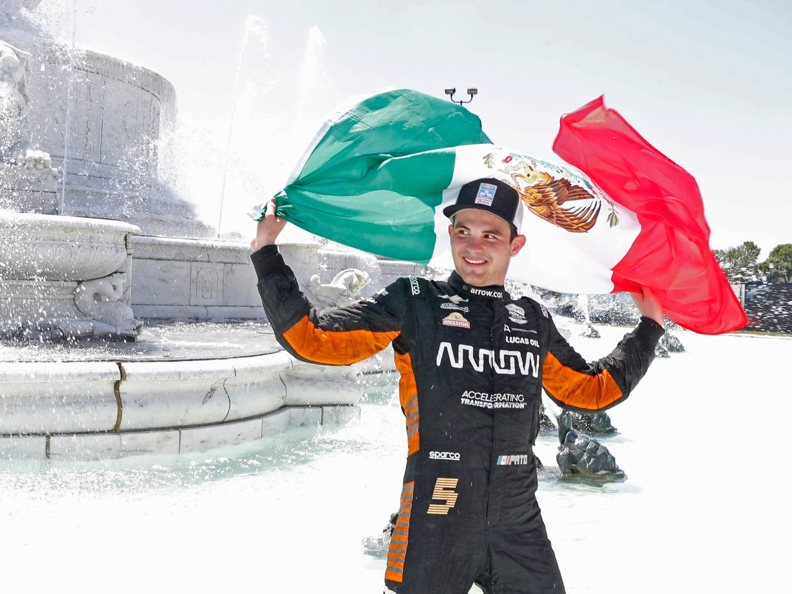 Pato O'Ward raises a Mexican flag while celebrating his win in the James Scott Memorial fountain