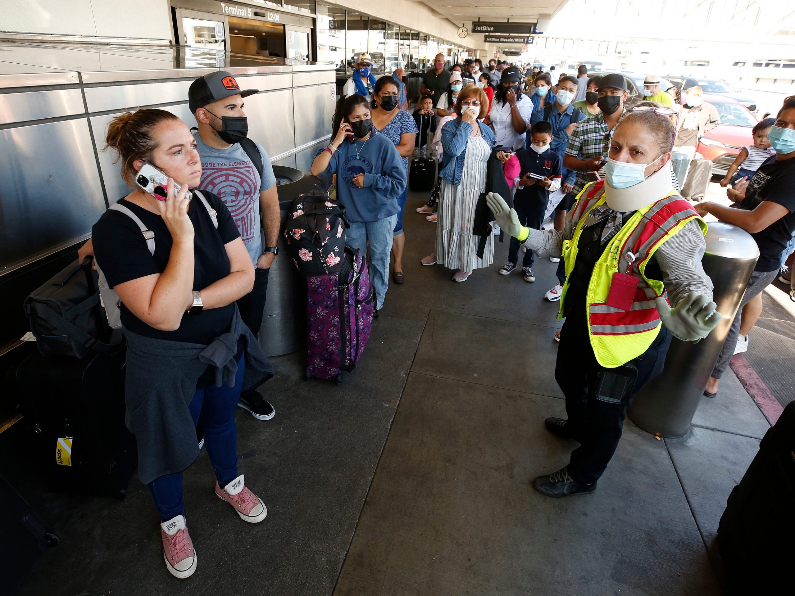 A customer service agent tries to calm passengers as they form a line that extends outside LAX Terminal 5 Tuesday morning as Spirit Airlines has canceled 313 flights on Monday, 40% of its scheduled flights, and 210 flights have been delayed.