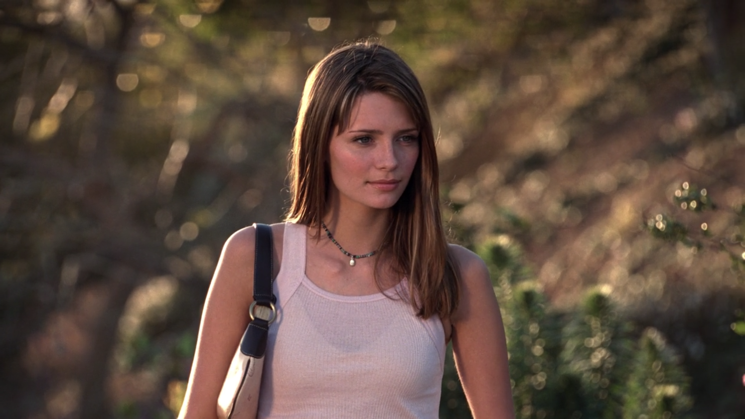 A brunette teenage girl stands outside while wearing a pink tank top.