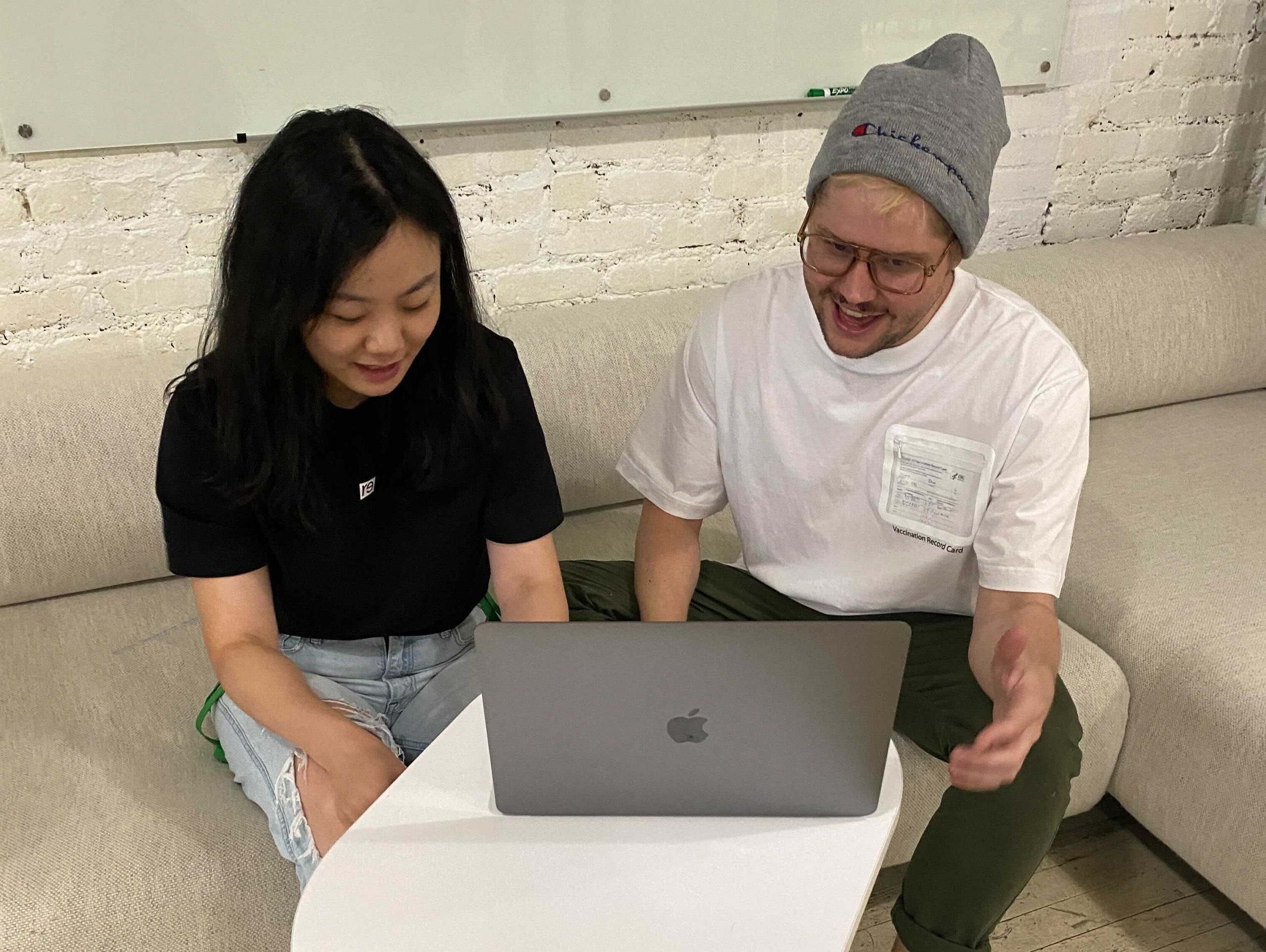 Woman and man wearing vaccine card shirt sit next to each other in front of laptop