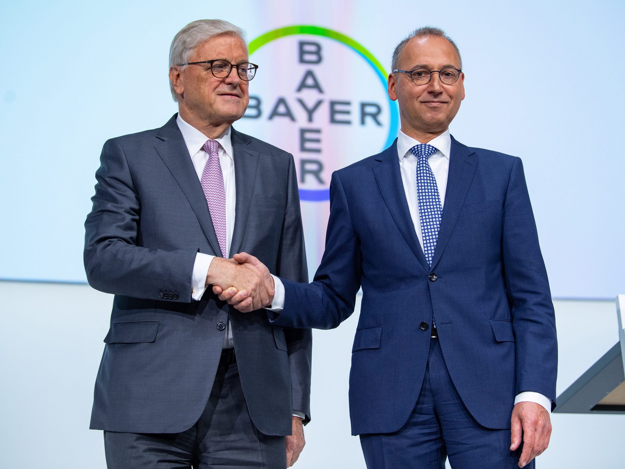 Werner Baumann, Chairman of the Board of Management of Bayer AG, and Werner Wenning, Chairman of the Supervisory Board of Bayer AG, stand on stage at the Bayer Annual Stockholders' Meeting and shake hands.