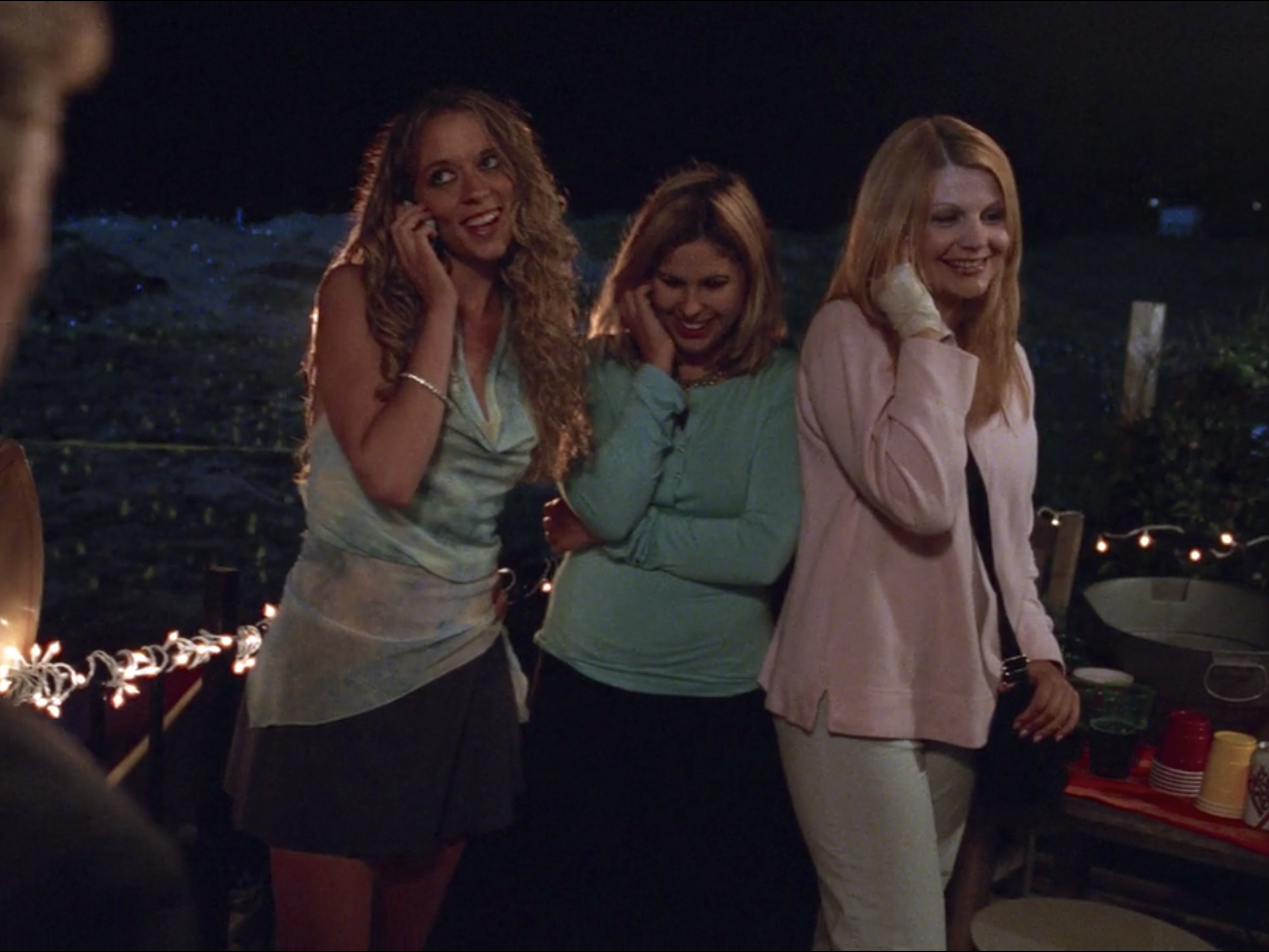 A group of teenage girls standing outside a party, each one holding a cell phone up to their ear.