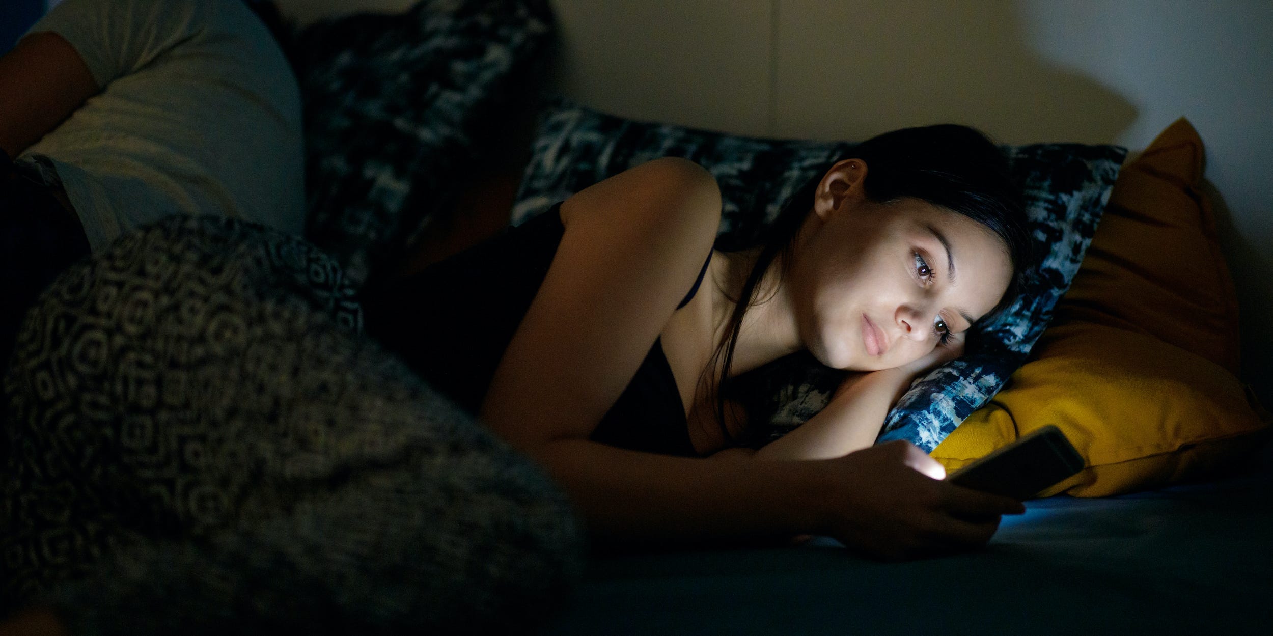 Woman laying in bed looking at phone dark at nighttime