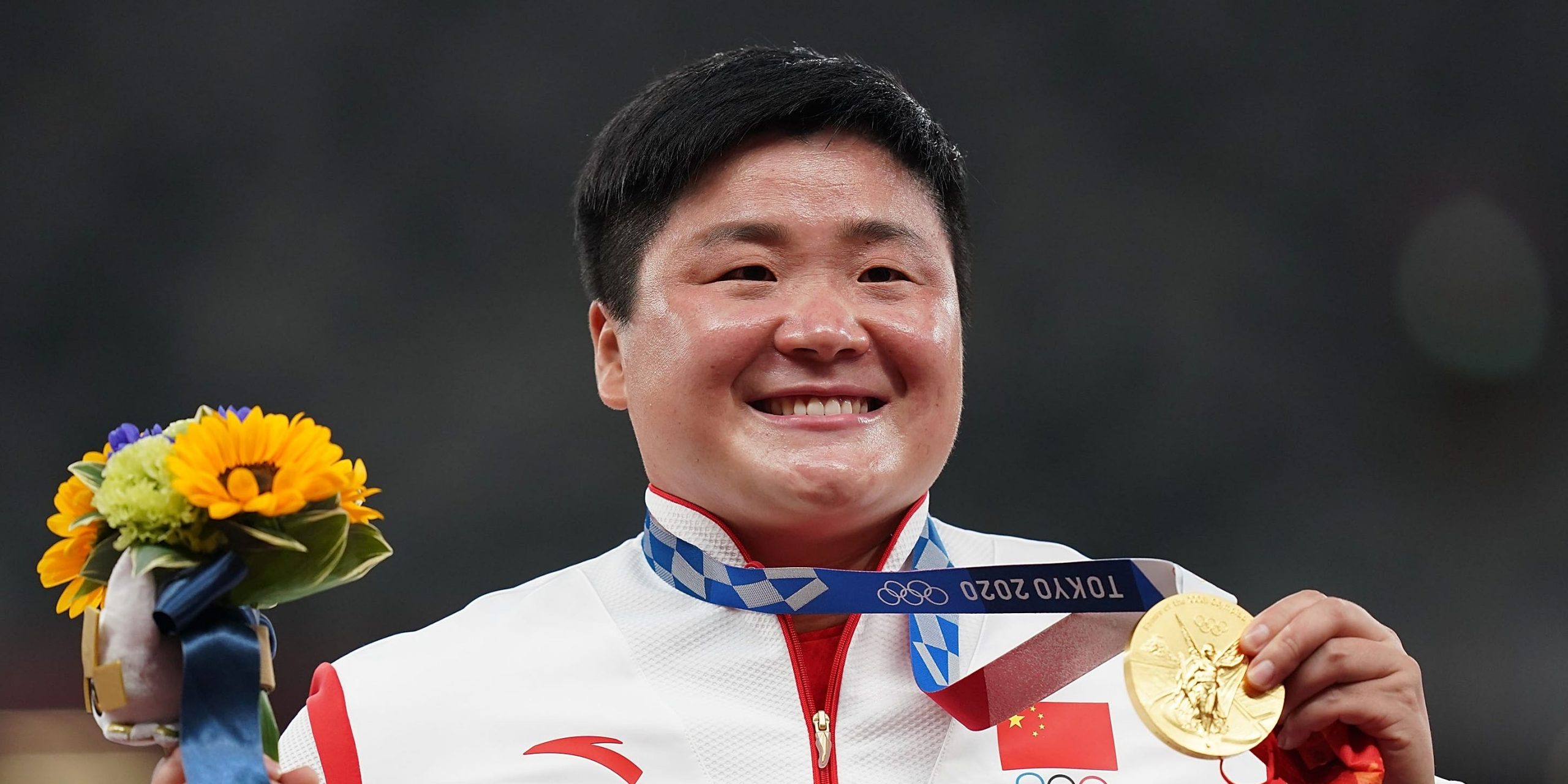 Gong Lijiao smiles as she holds a bunch of flowers and the gold medal around her neck