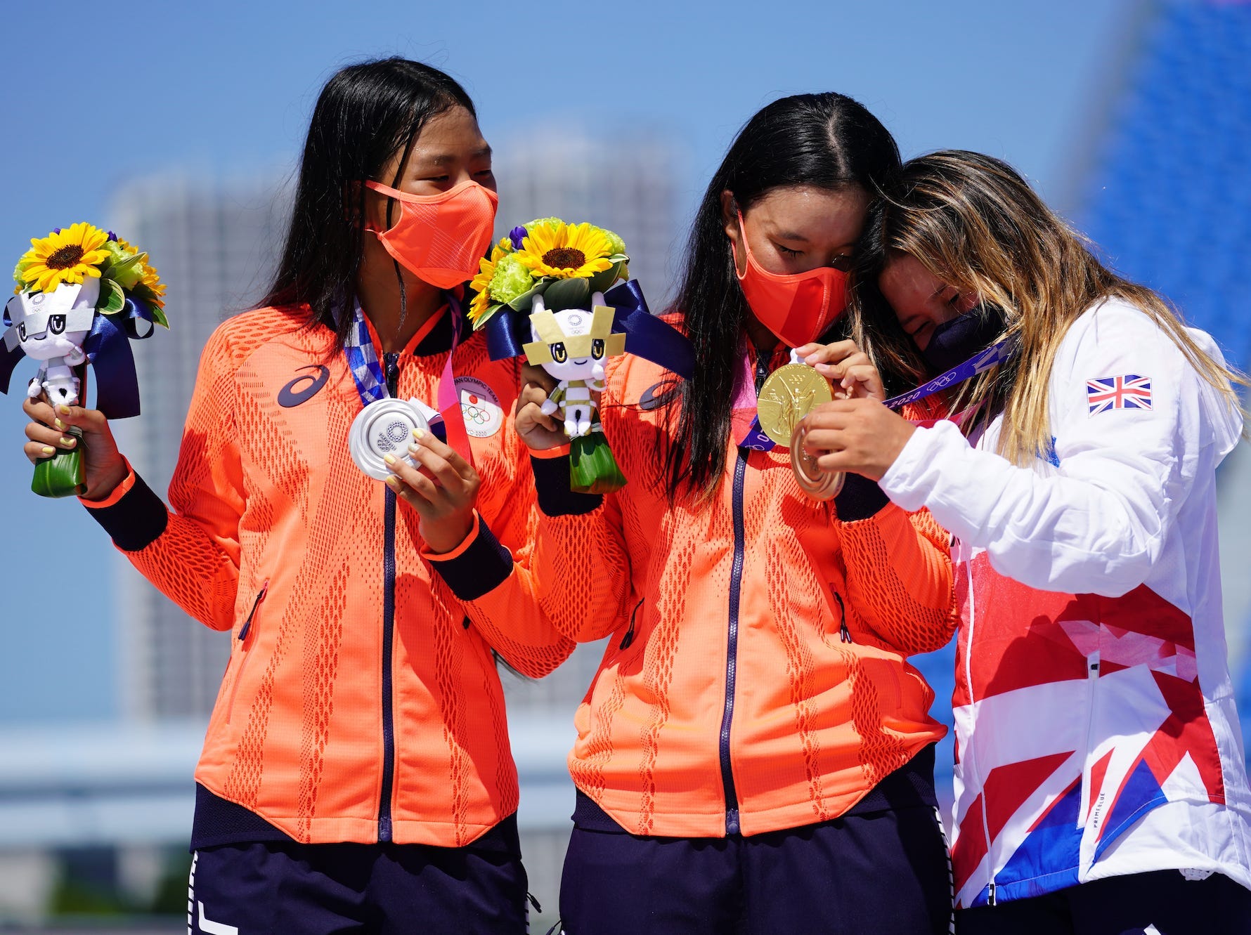 Sky brown leans her head on Sakura Yosozumi as she holds her medal on the podium with Sakura Kokona Hiraki