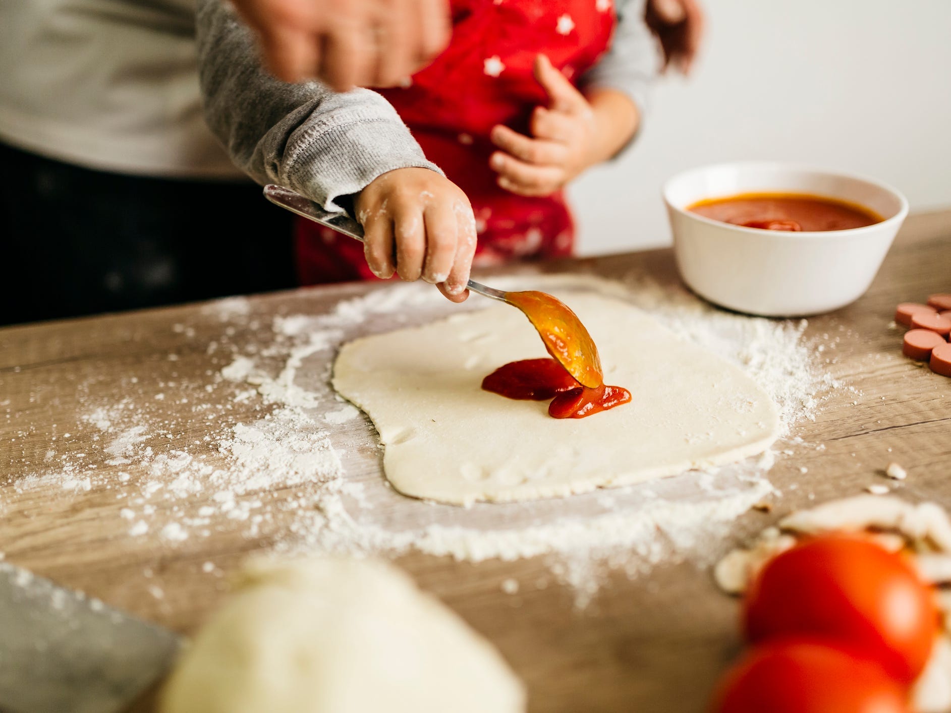 A child spreading pizza sauce on pizza dough.