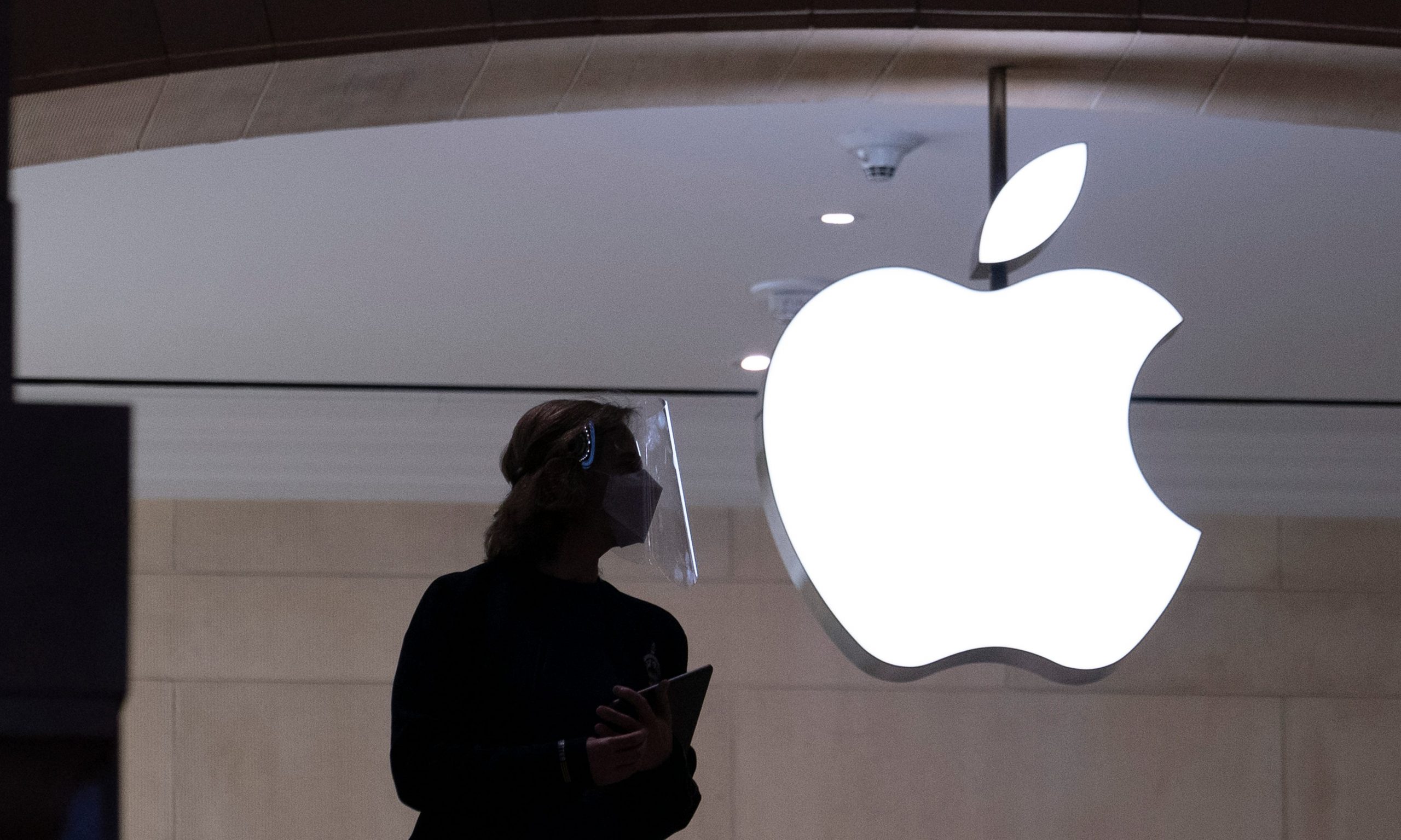 An Apple store employee's dark silhouette next to a white glowing Apple logo