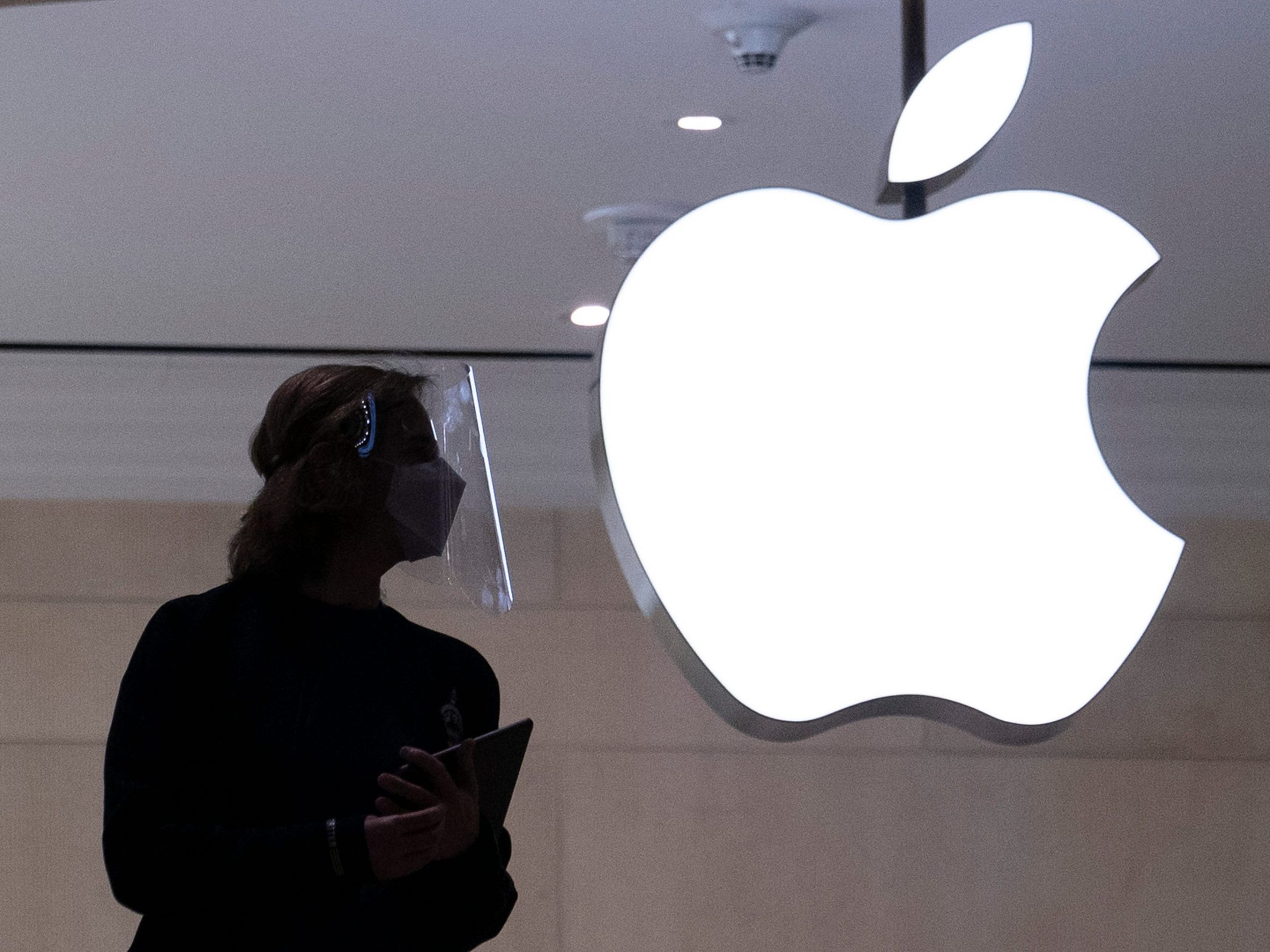 An Apple store employee's dark silhouette next to a white glowing Apple logo