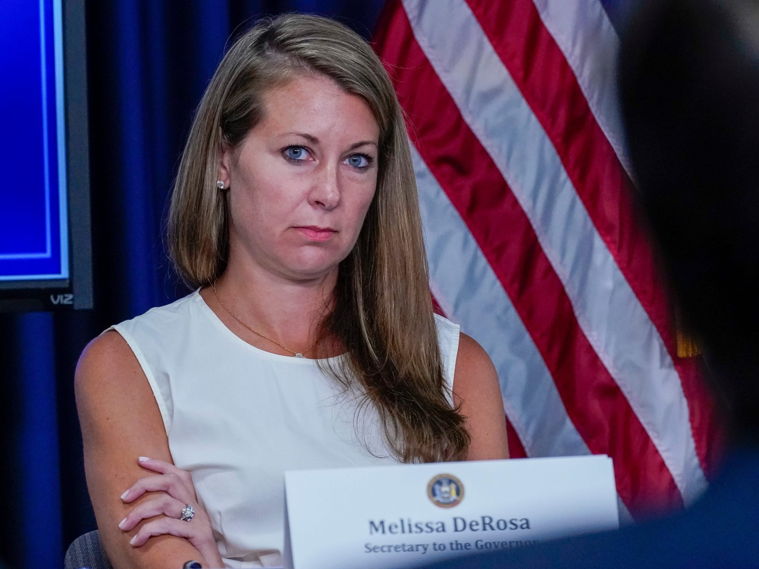 Secretary to the Governor Melissa DeRosa listens as New York Gov. Andrew Cuomo speaks to reporters during a news conference, Wednesday, June 23, 2021, in New York. She is wearing a white dress and has her arms crossed.