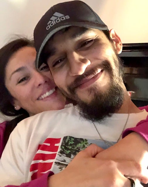A woman hugging a man from behind as they both smile at the camera.
