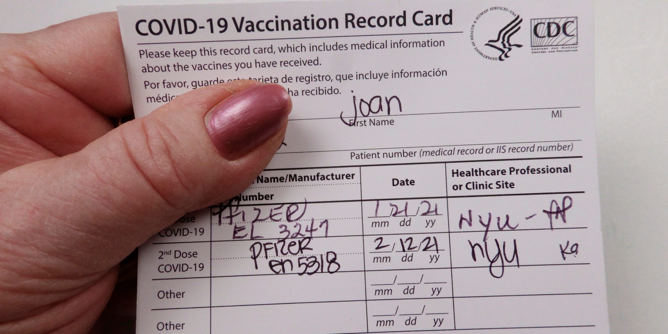 A hand holding a CDC card that reads "COVID-19 Vaccination Record Card"