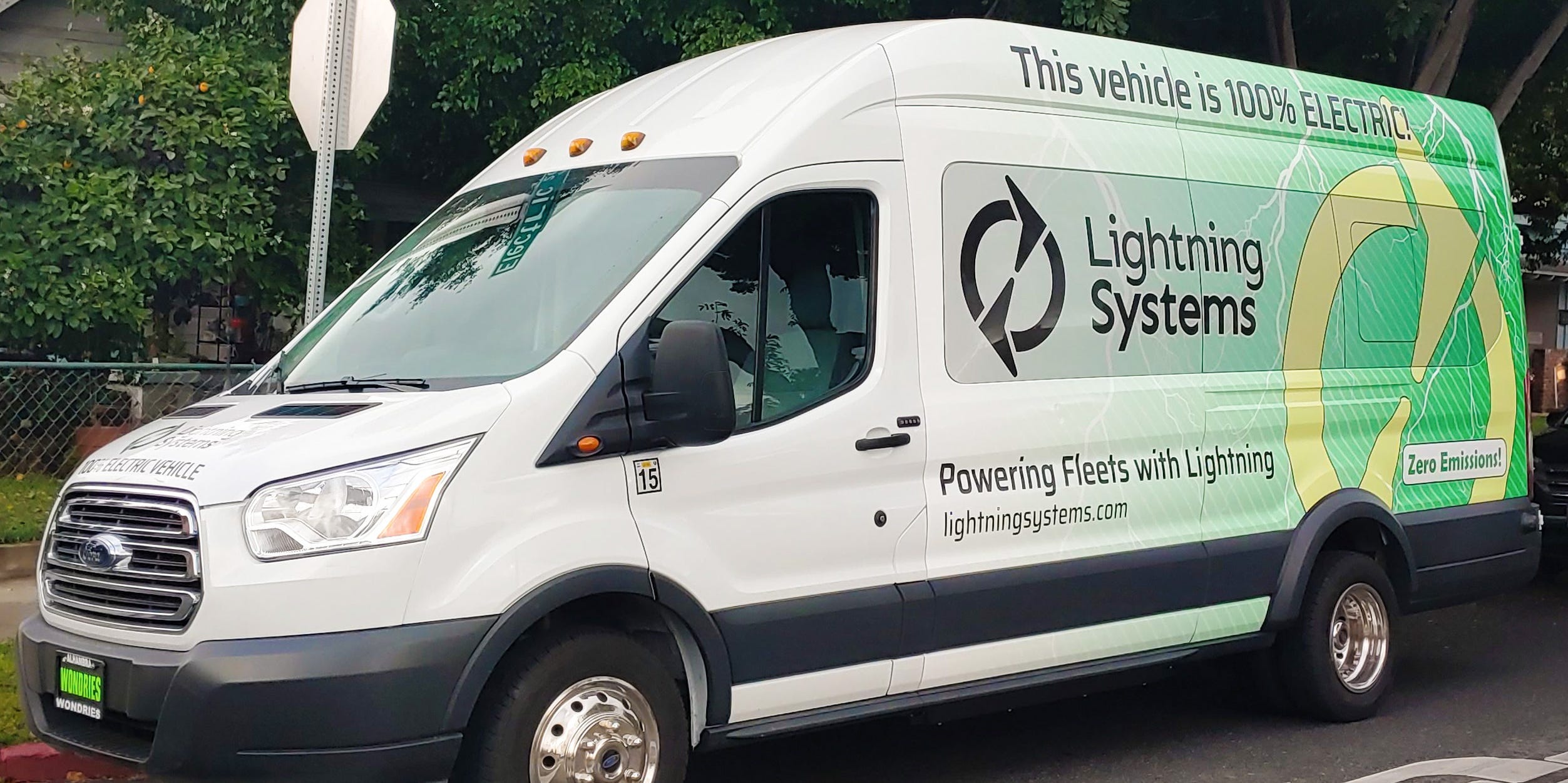 A white electric-powered van sits on a street corner.