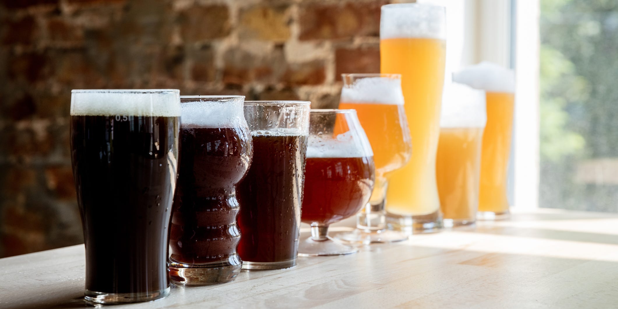 Several pints of beer in different shaped glasses arranged in order from dark to light