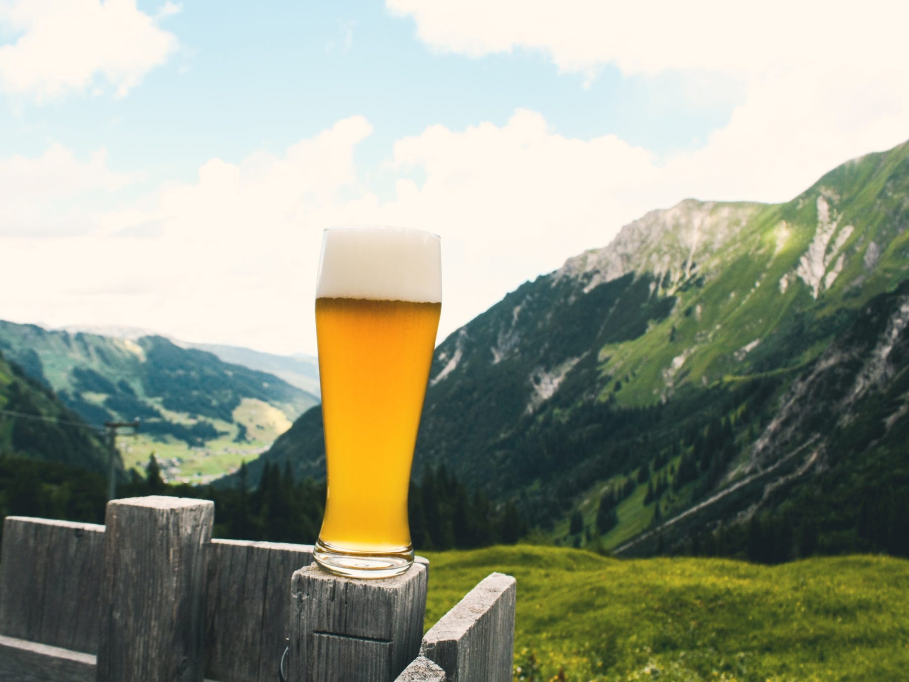 A pint of beer sitting on a wooden fence post with a beautiful rolling mountainside in the background