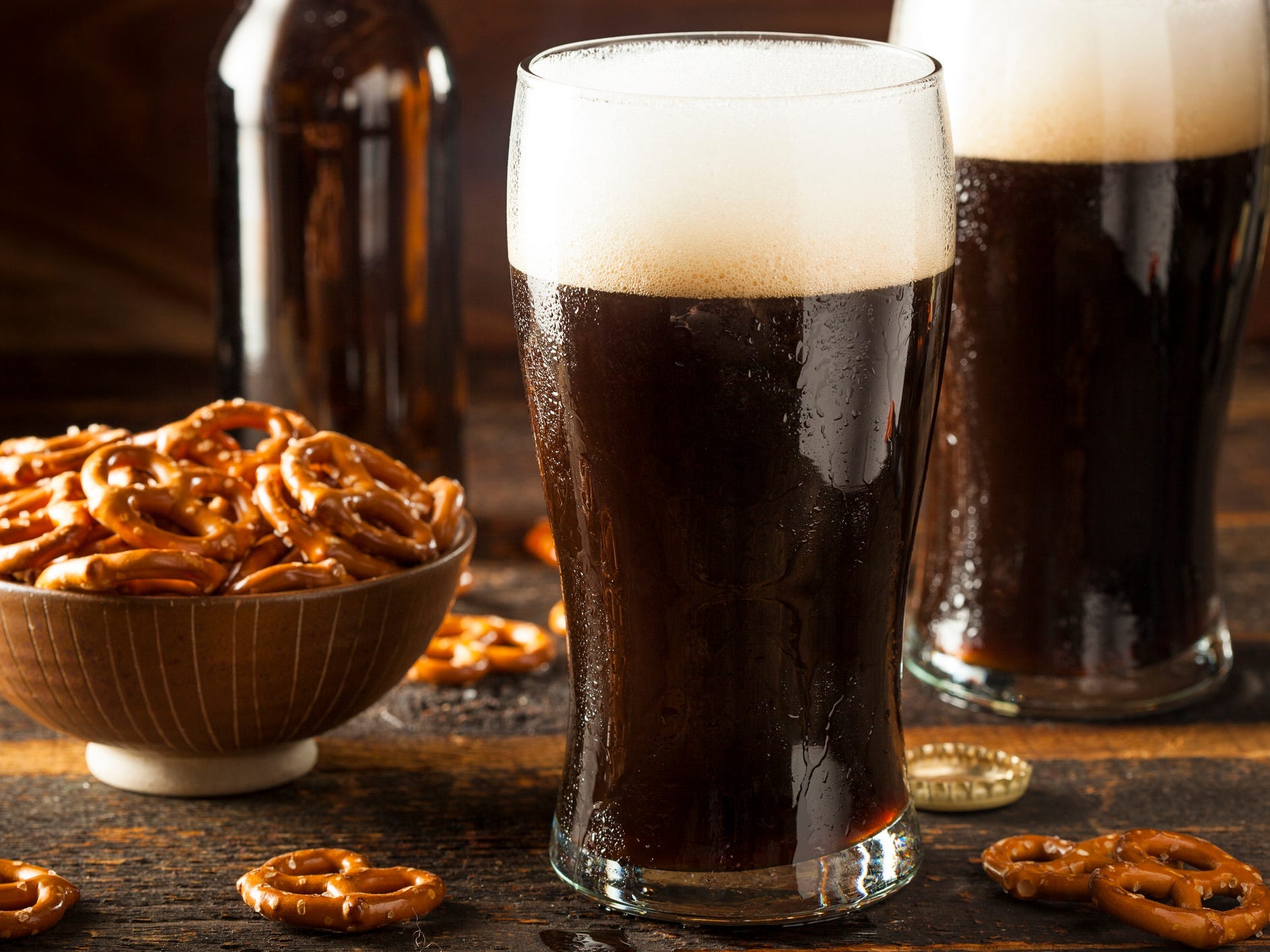 Two pints of stout beer next to a bowl of pretzels