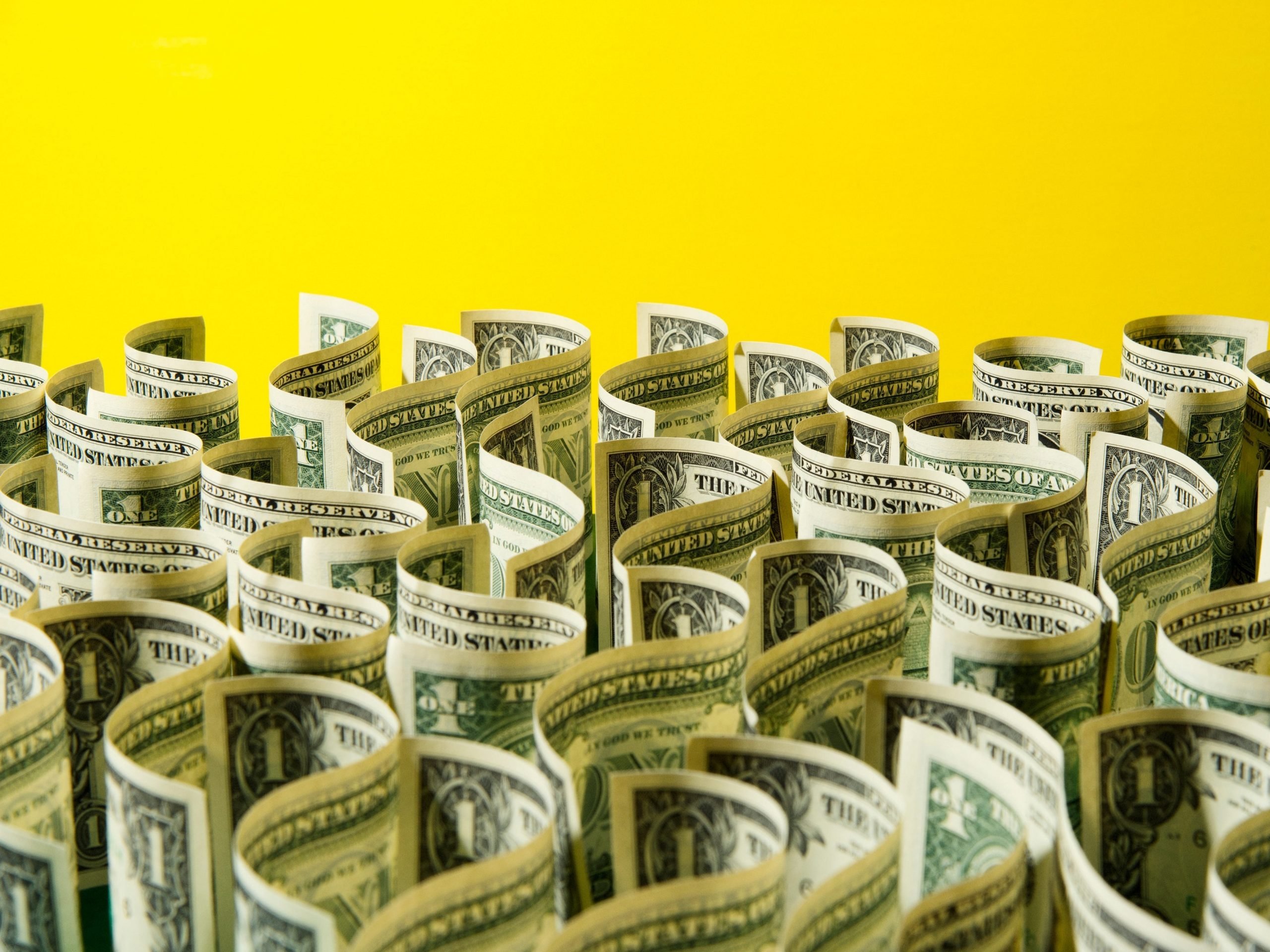 wavy dollar bills against a bright yellow background