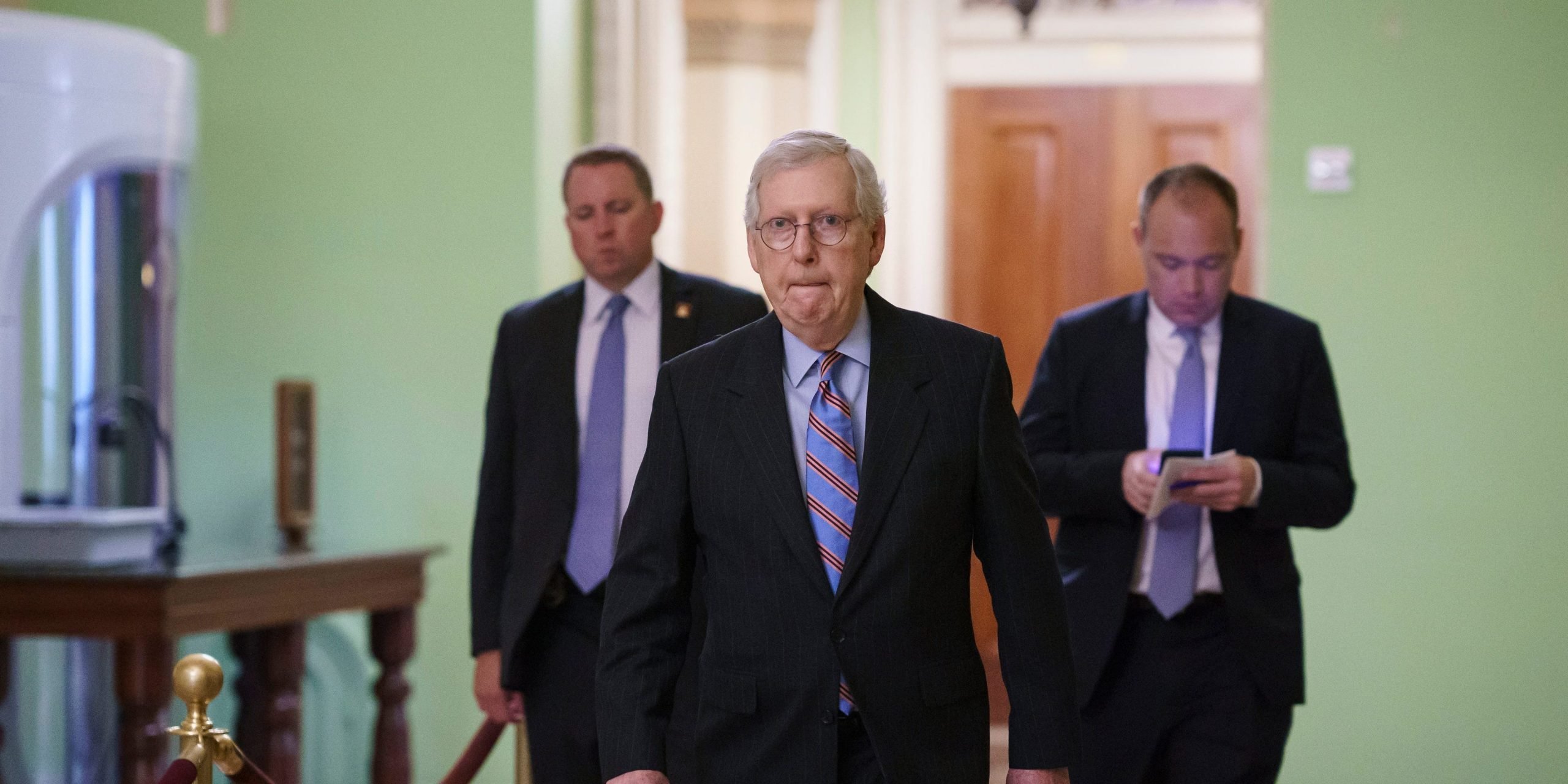 Mitch McConnell walks down a hallway.