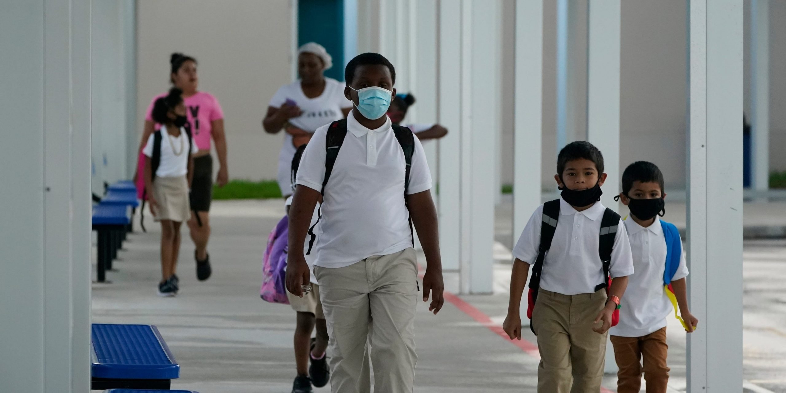 Children in masks walk down a school hallway.