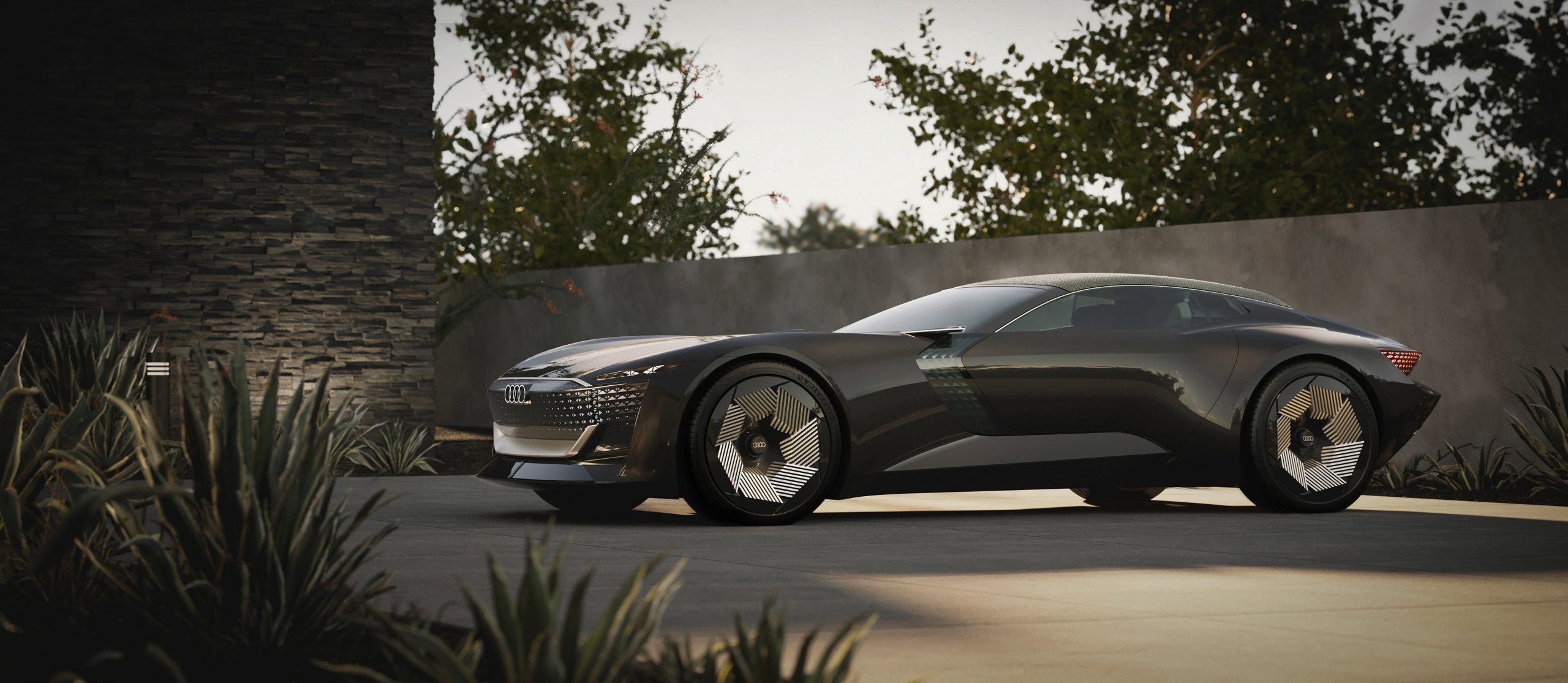 A sleek black Audi vehicle with big silver wheels sits on a driveway.