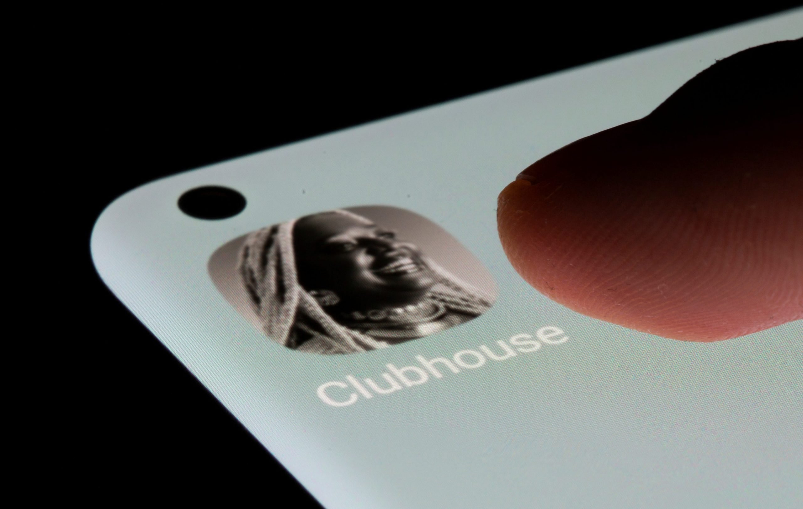 A finger taps the Clubhouse app icon on a bright iPhone screen