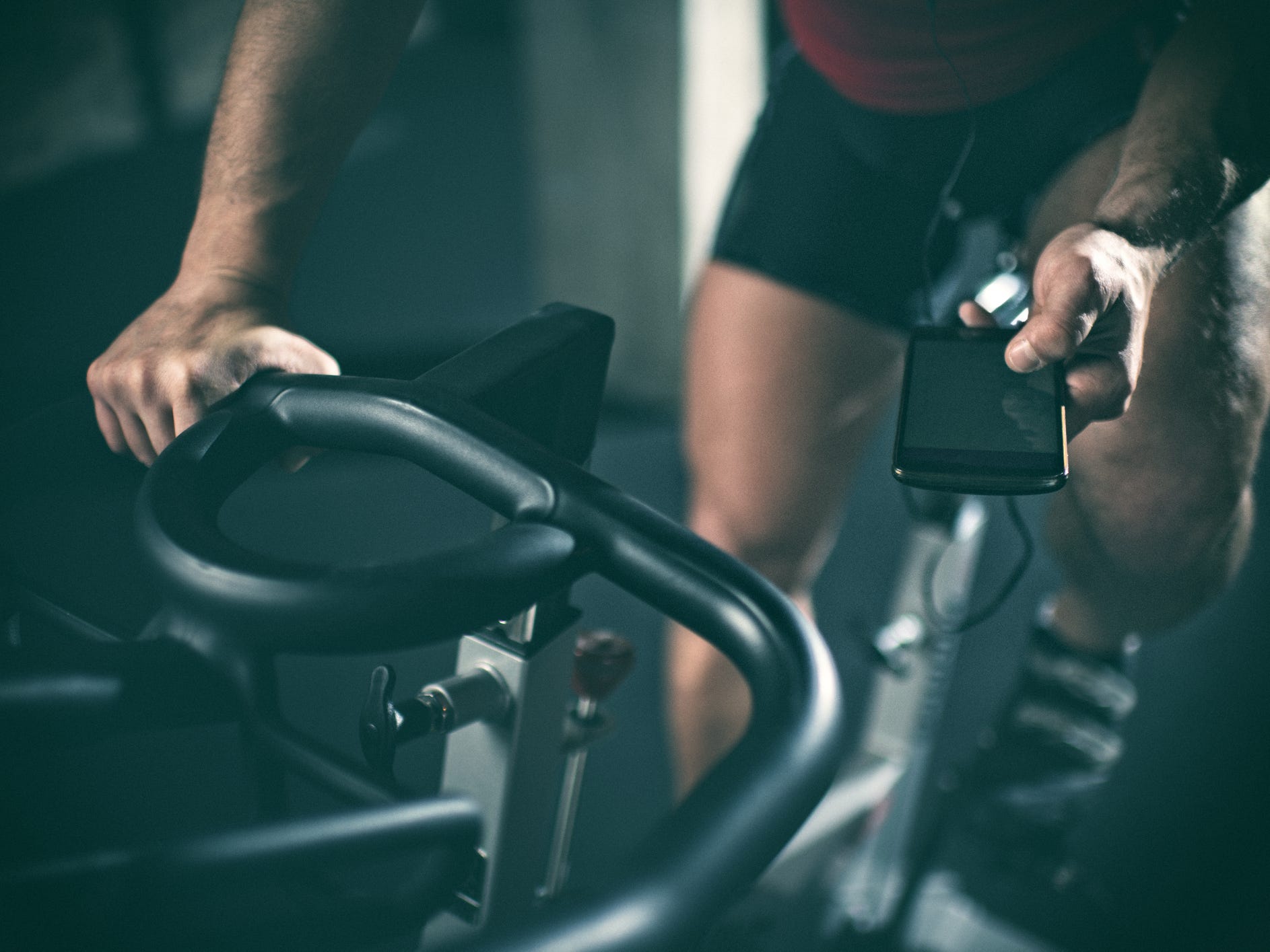 an athlete checking a phone and grasping the handbags of a stationary bicycle with legs poised to pedal