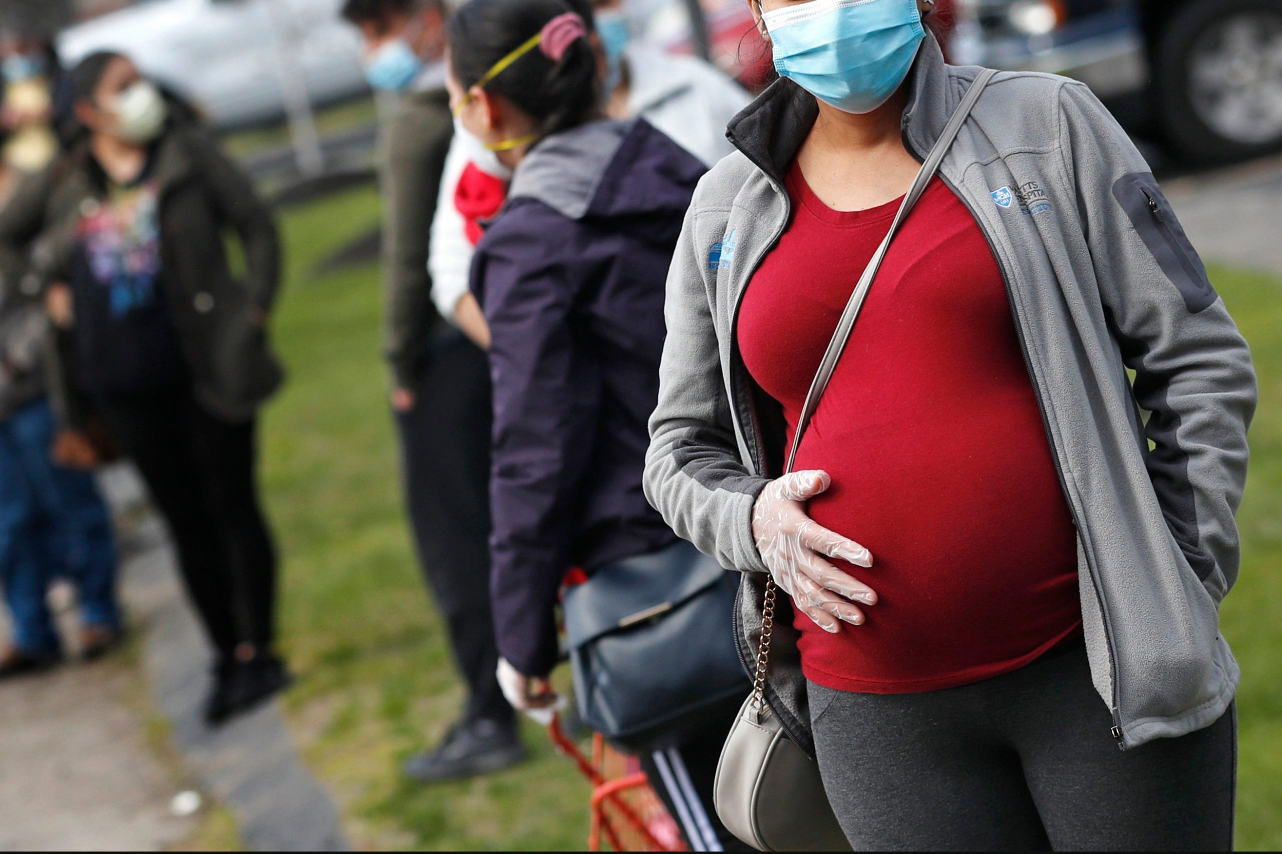 A masked pregnant woman holding her stomach