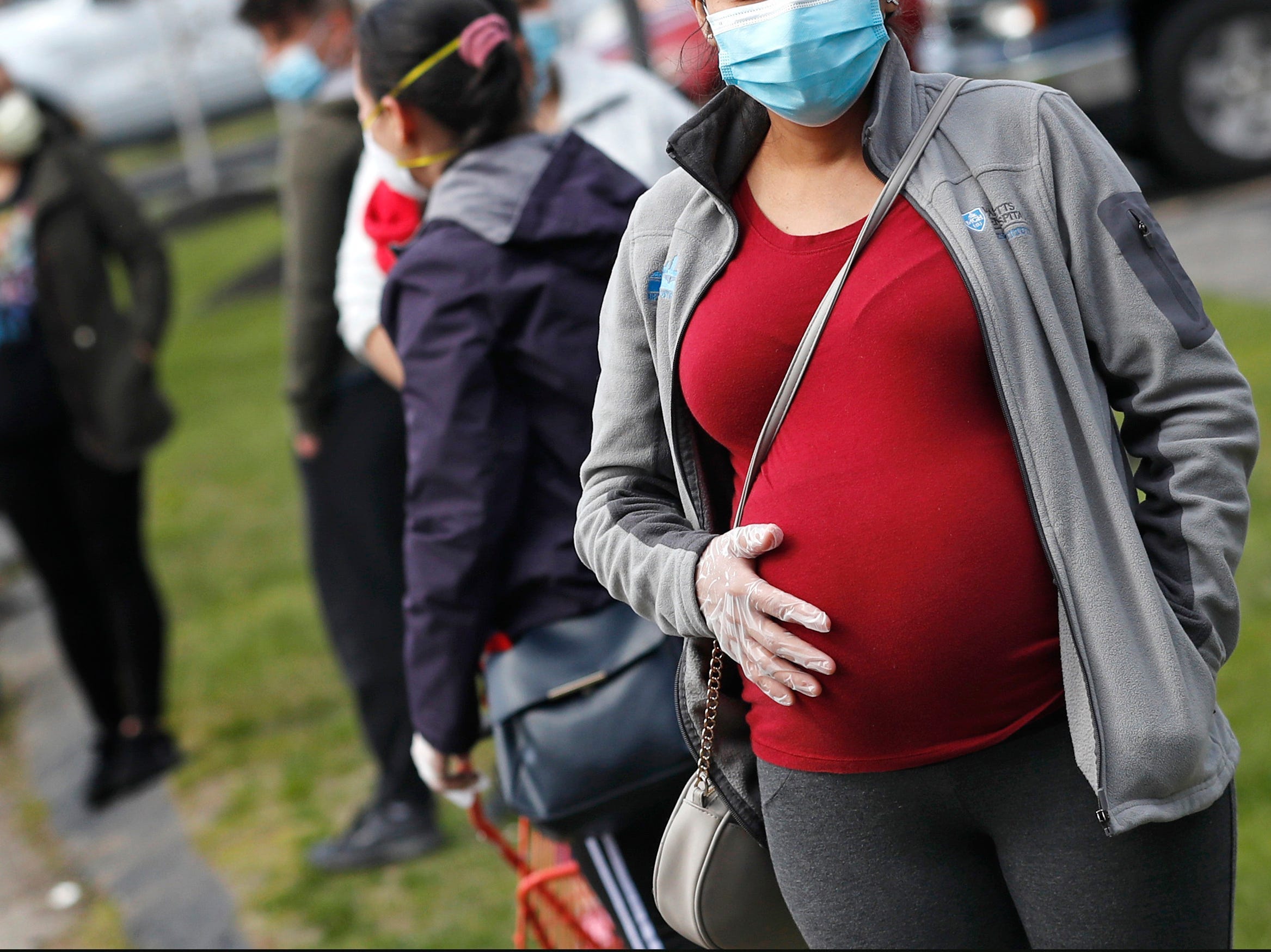 A masked pregnant woman holding her stomach