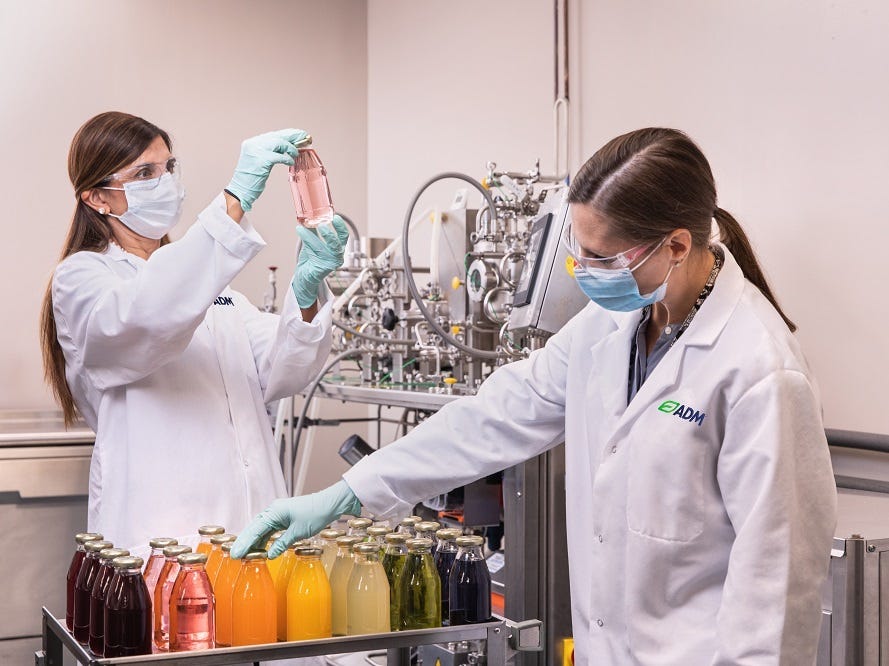 two women in lab coats bottle juices in a lab