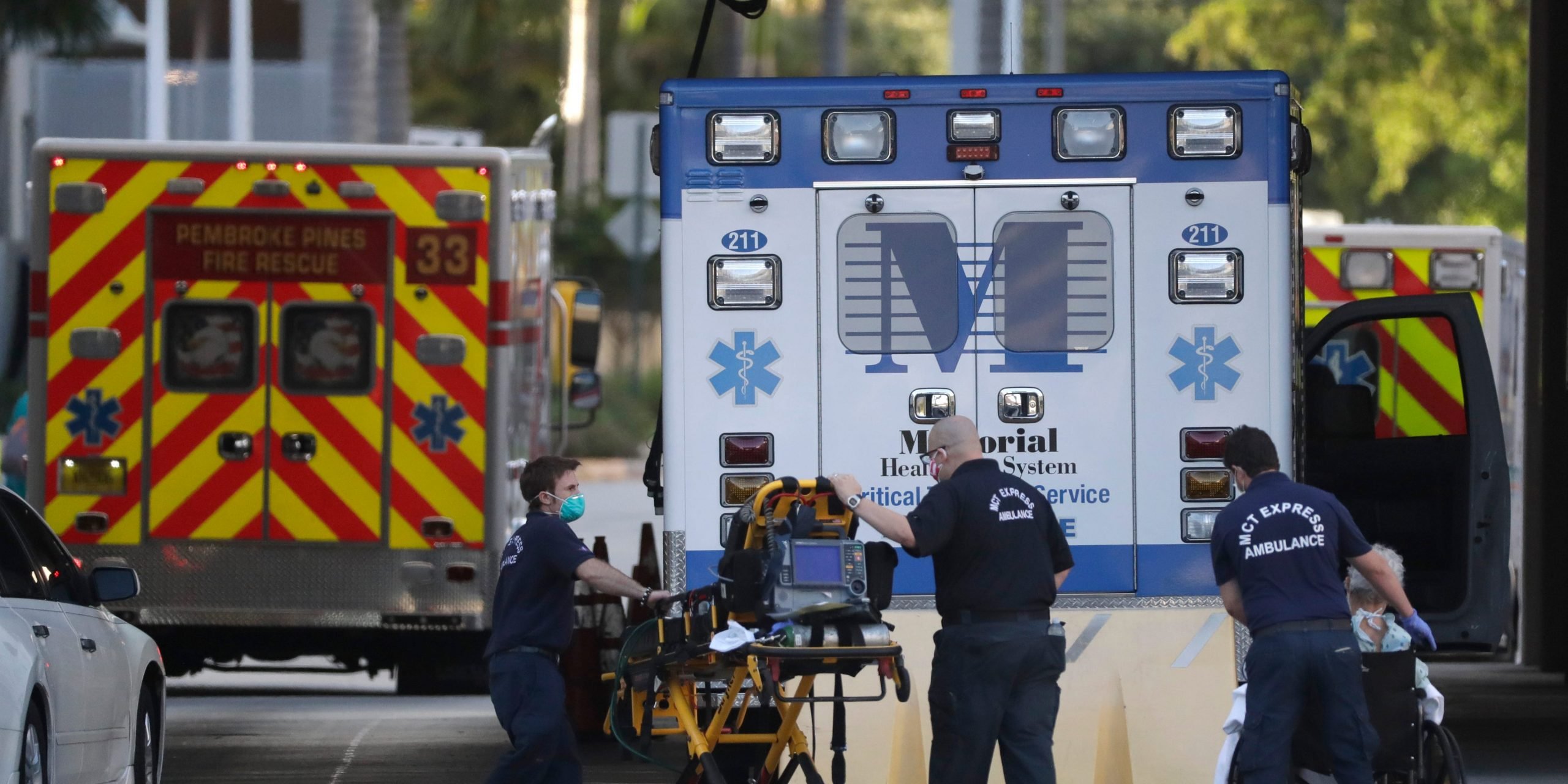 Emergency responders stand in front of an ambulance.