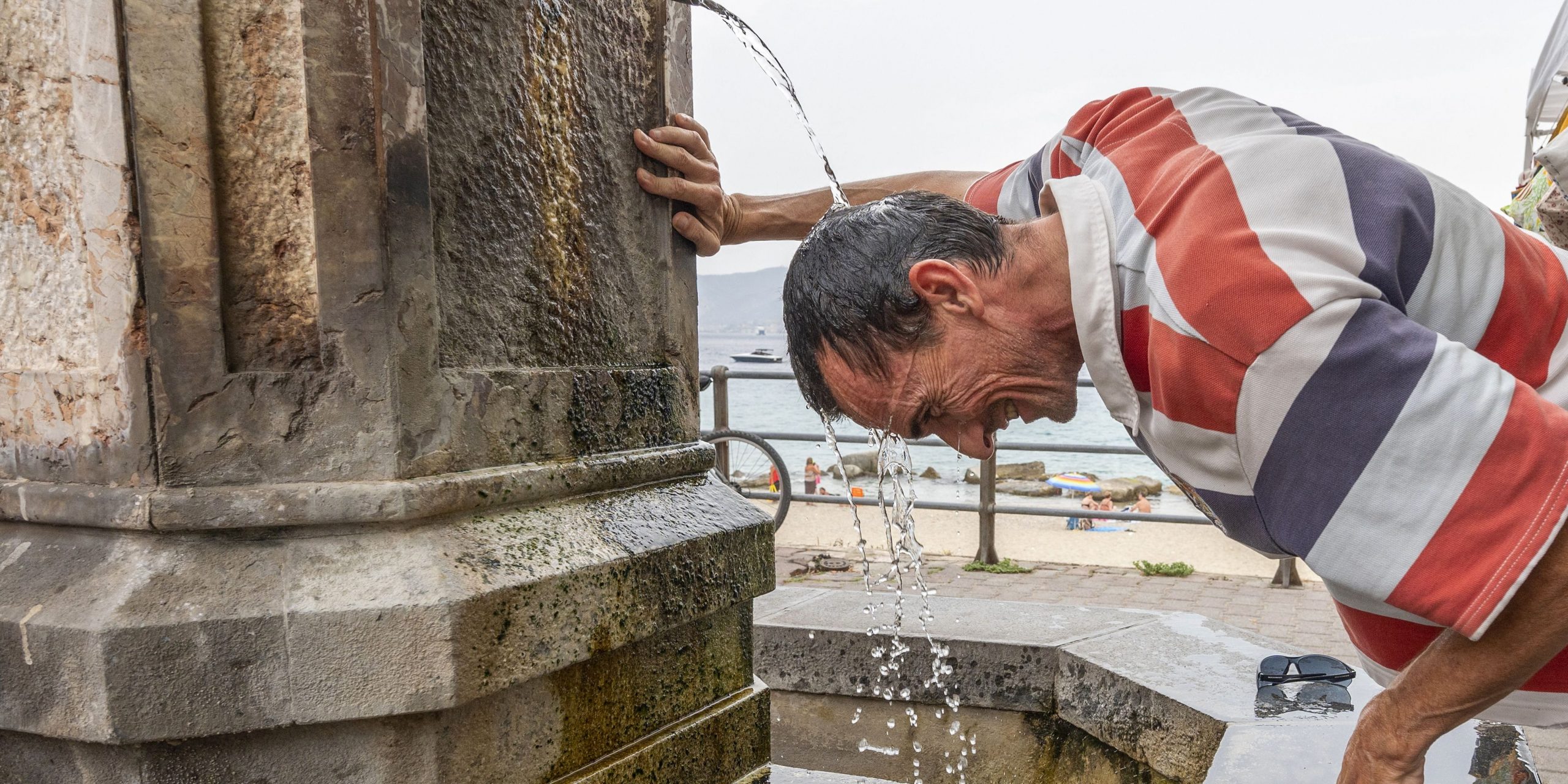 A man refreshes himself in a fountain during a hot summer day in Messina, Sicily, on August 11, 2021