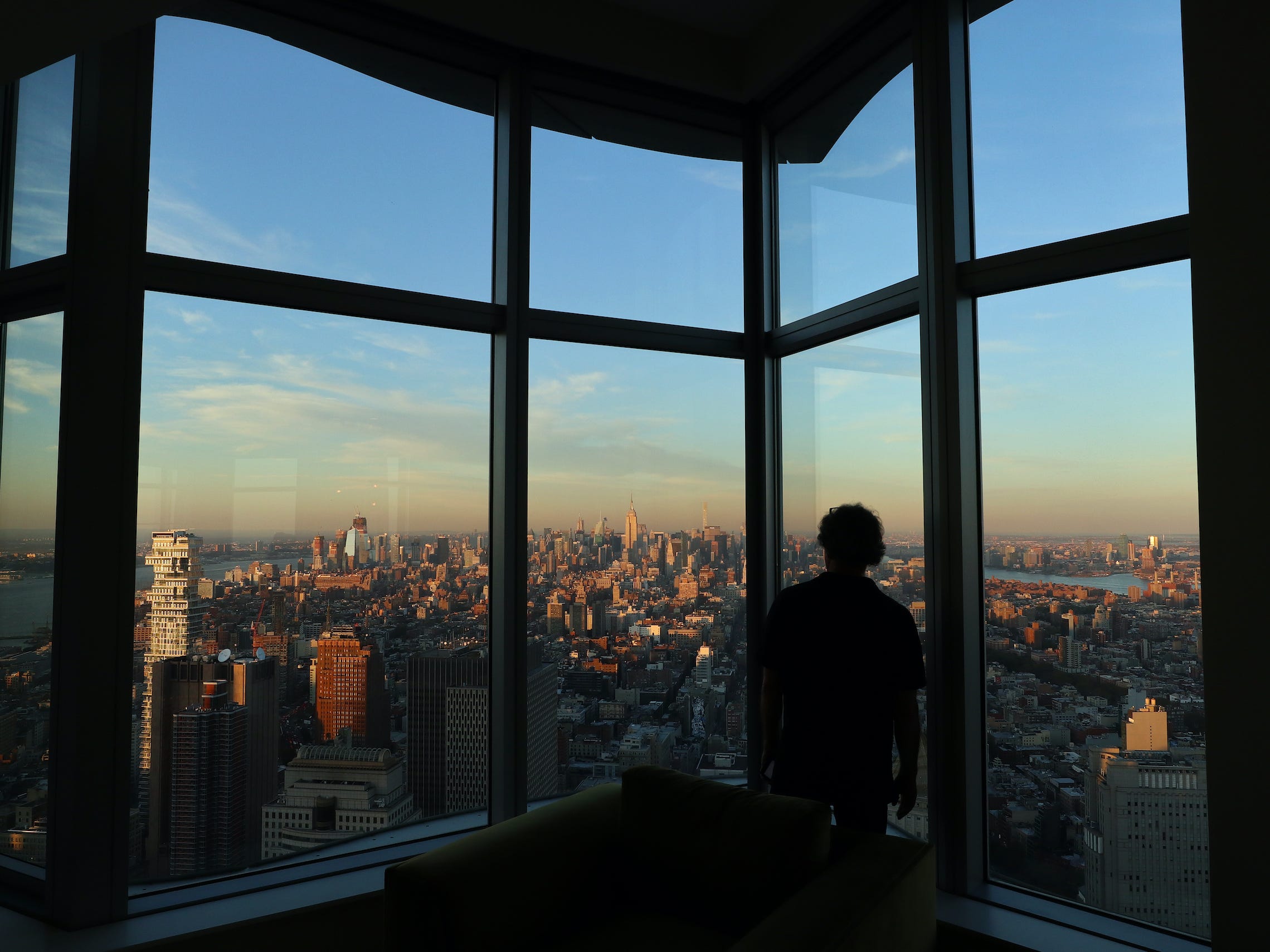 Man standing in penthouse window at sunset overlooking New York City skyline