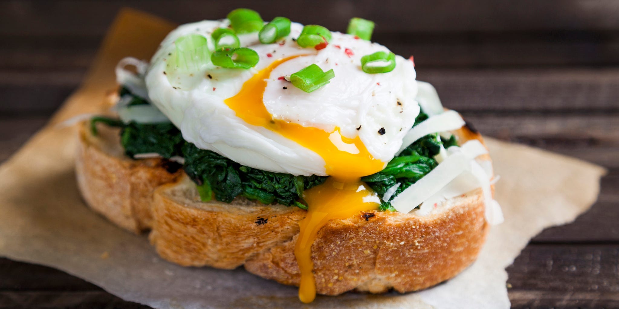 A poached egg with the yolk spilling out atop a piece of toast topped with spinach