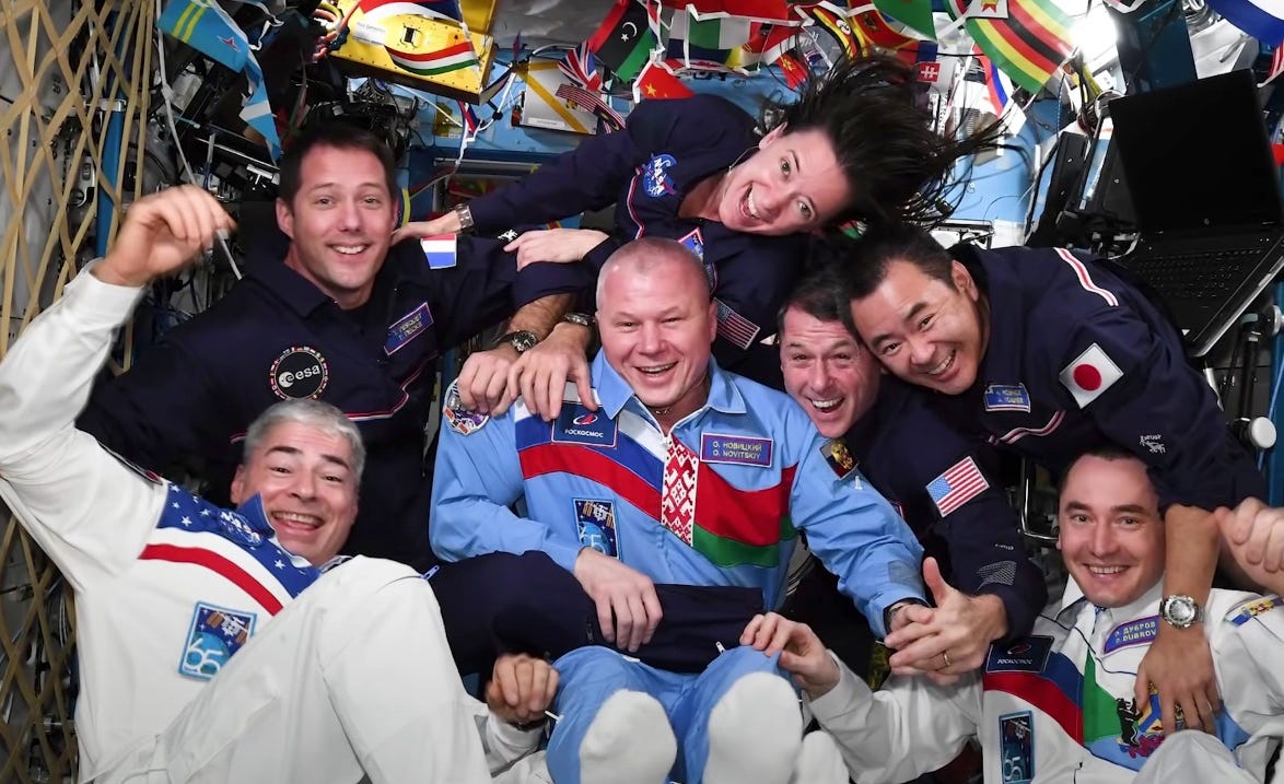 seven astronauts crowded together smiling on space station