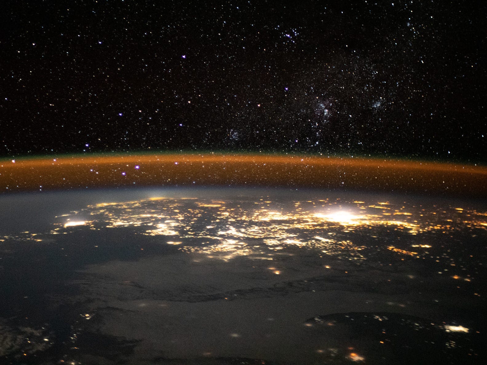 thin atmosphere glowing orange against space stars above nighttime earth city lights