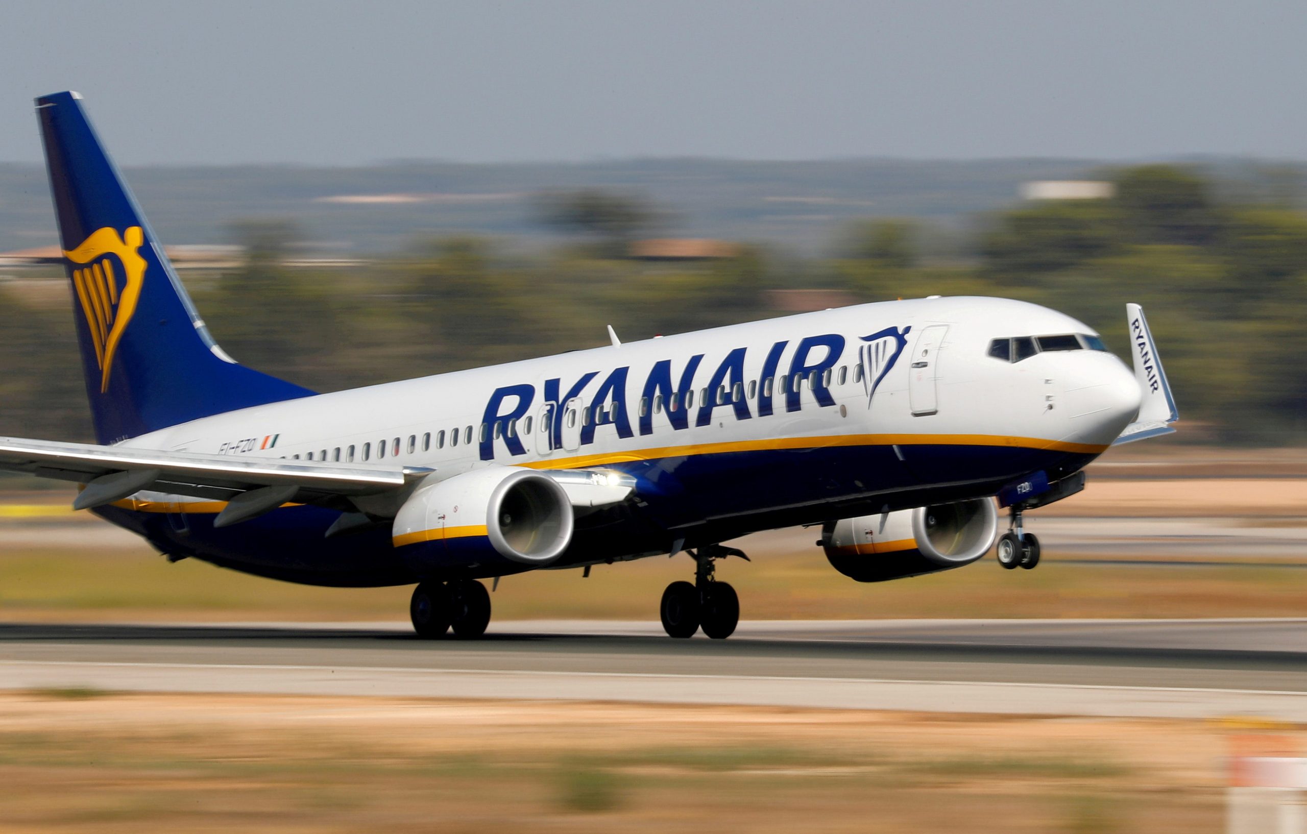 A blue, white, and yellow Ryanair plan takes off from the runway.
