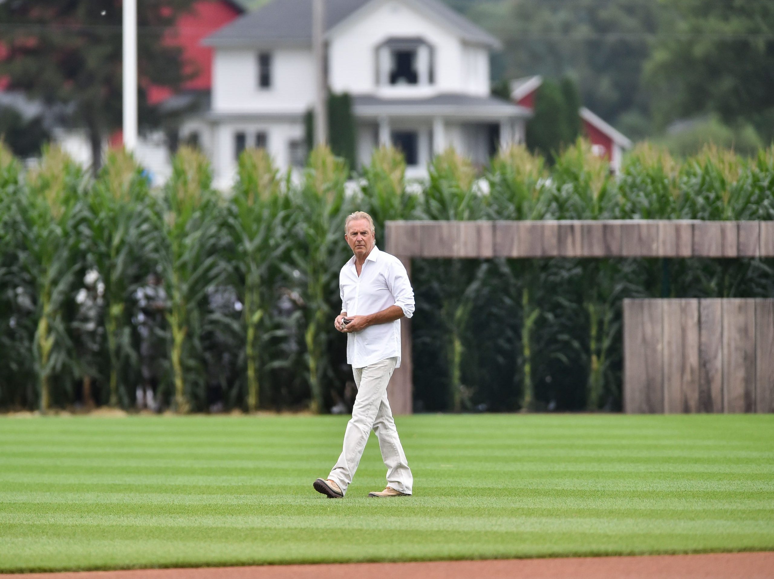 Kevin Costner dressed in white walking on The Field of Dreams baseball field