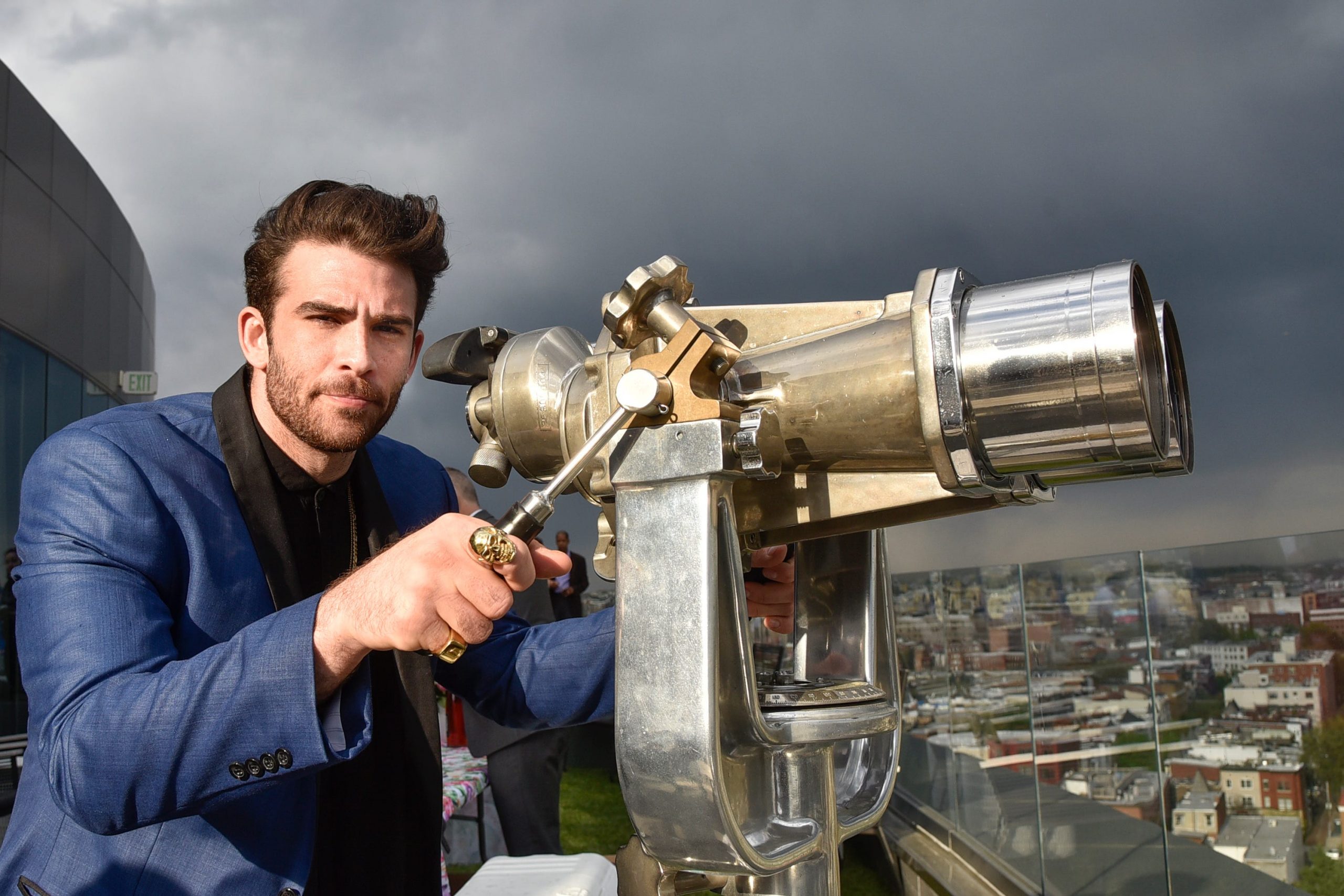 Hasan Piker wears a blue jacket and looks upon a city.