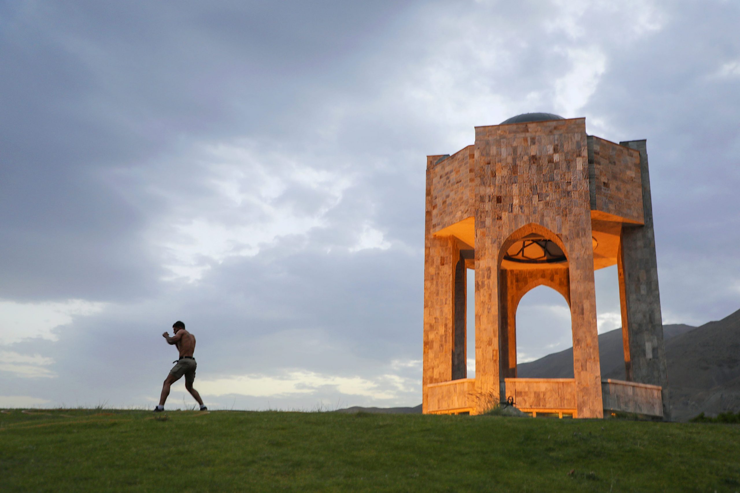 A man is seen, at a distance, shadowboxing near a mausoleum.