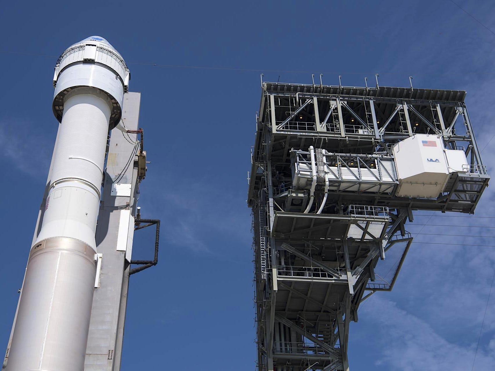 rocket with starliner spaceship atop next to launch tower against blue skies