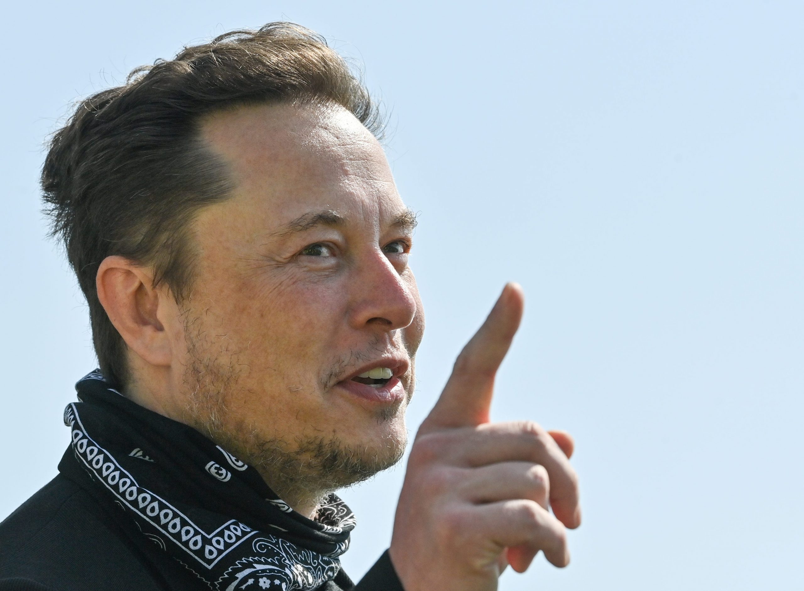 Tesla CEO Elon Musk points a finger upward while wearing a black bandana around his neck