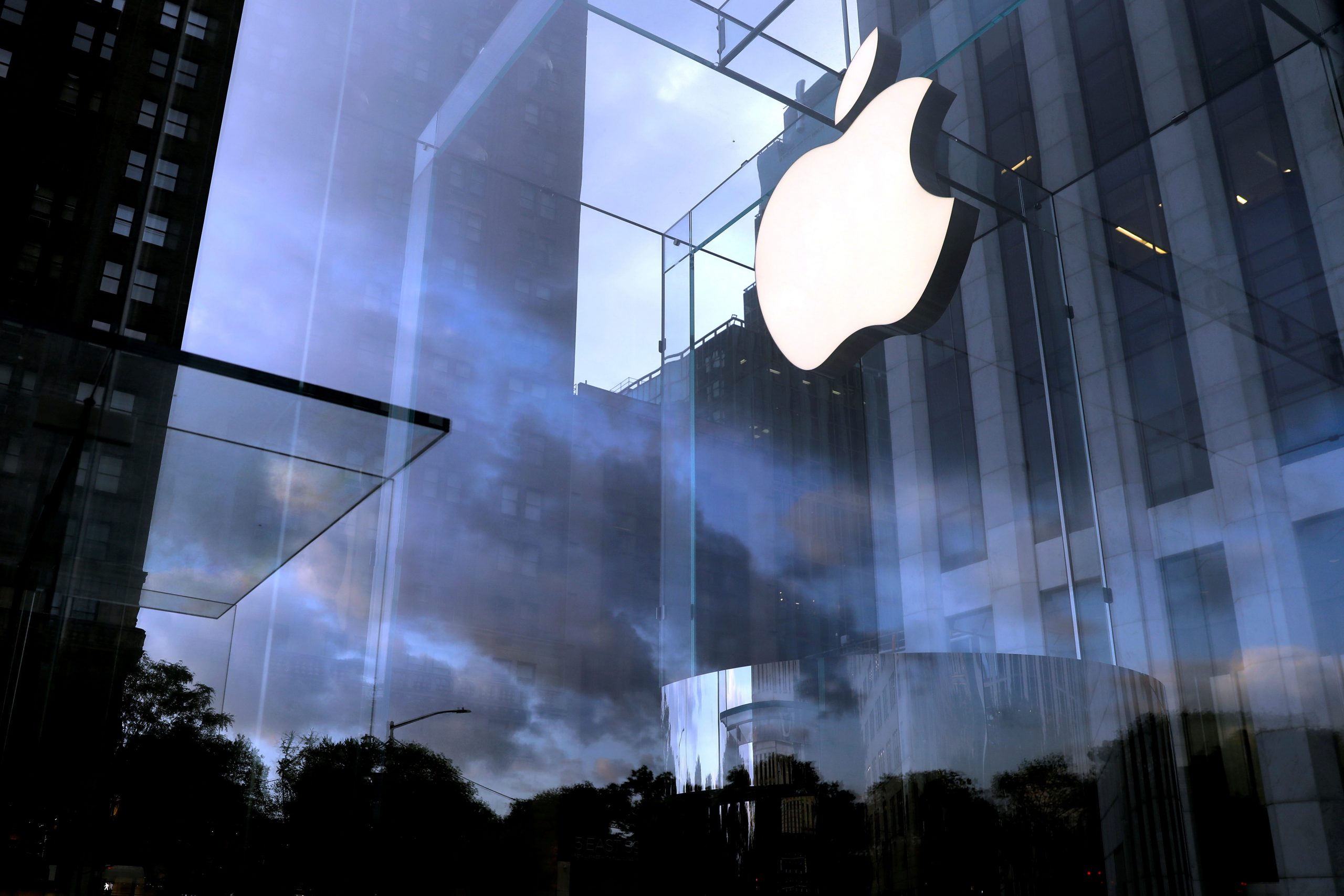 A cloudy sky behind a brightly lit Apple logo in a Manhattan store