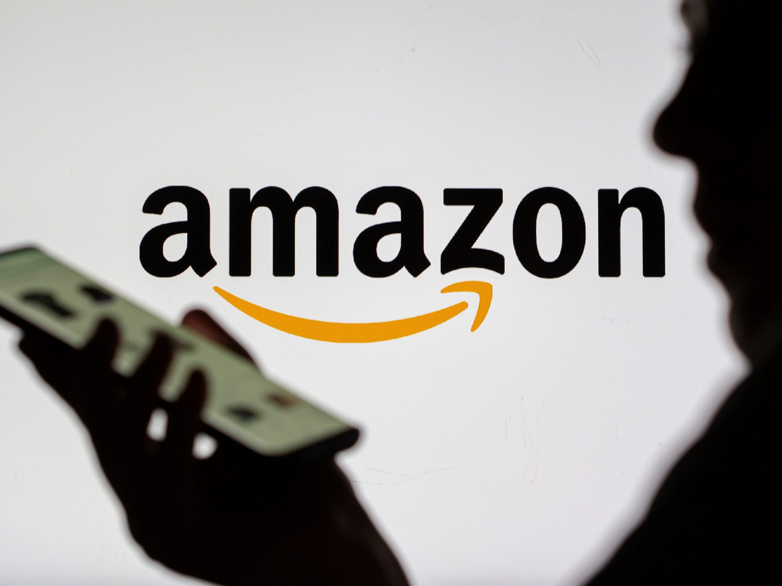 Silhouette of a person holding a phone, with the Amazon logo in the background