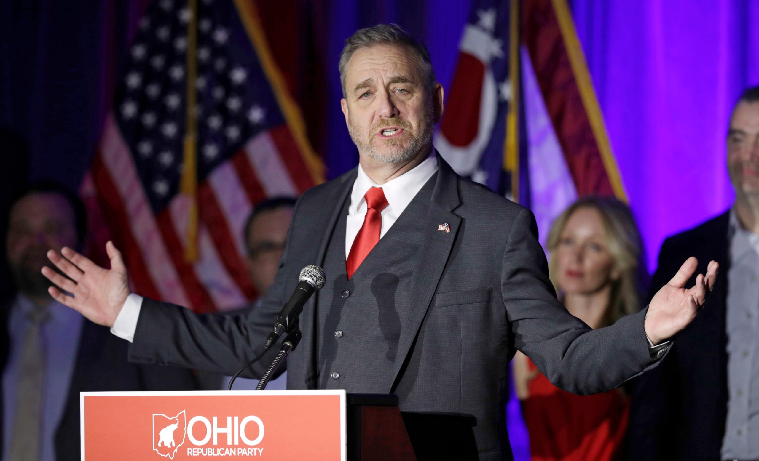 Ohio Attorney General Dave Yost in a suit raises his arms as he speaks to a crowd