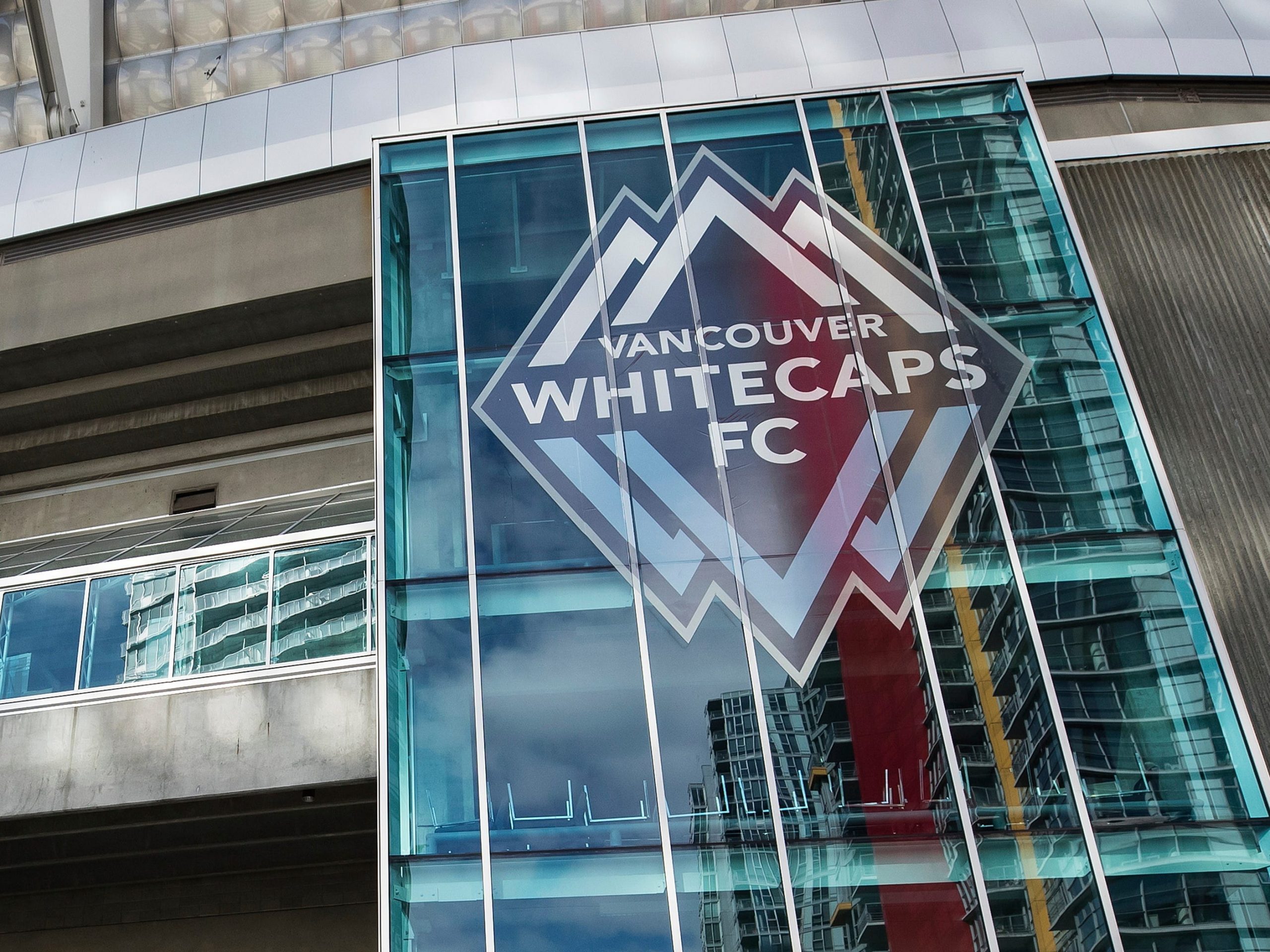 A worker cleans a door handle at B.C. Place stadium, where Major League Soccer's Vancouver Whitecaps play their home games, in Vancouver, British Columbia, Thursday, March 12, 2020. Major League Soccer is shutting down for 30 days because of the coronavirus, the league announced Thursday. (Darryl Dyck/The Canadian Press via AP)